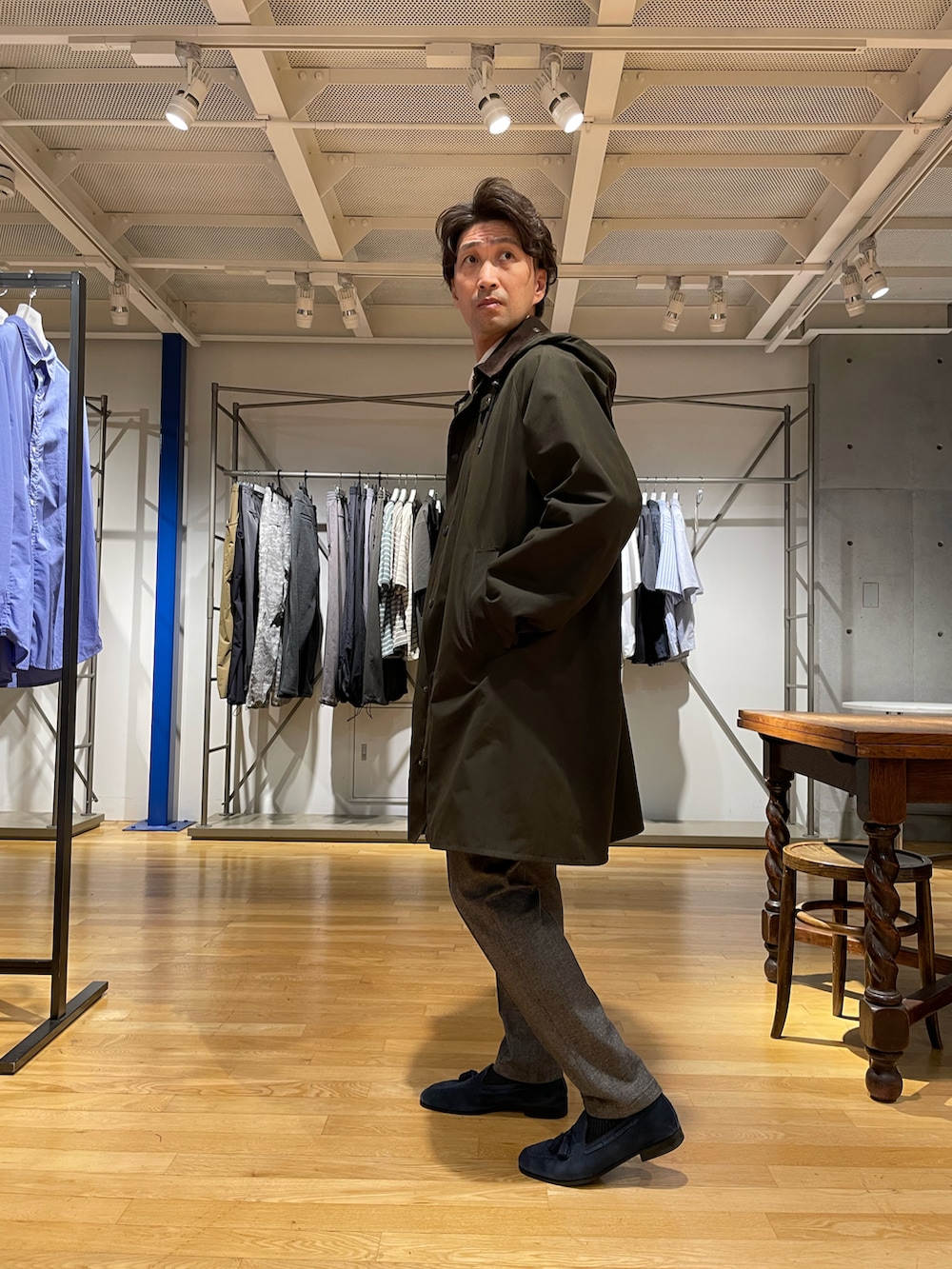 グリーン系のステンカラーコート、グレー系のスラックス、ホワイト系のパーカーを着用したメンズの秋コーディネートの2枚目の写真