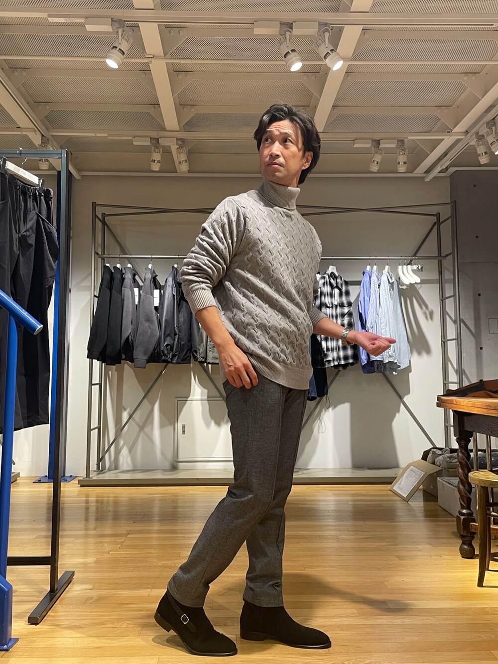 グレー系のニット/セーター、グレー系のスラックス、ブラック系のブーツを着用したメンズの秋コーディネートの2枚目の写真