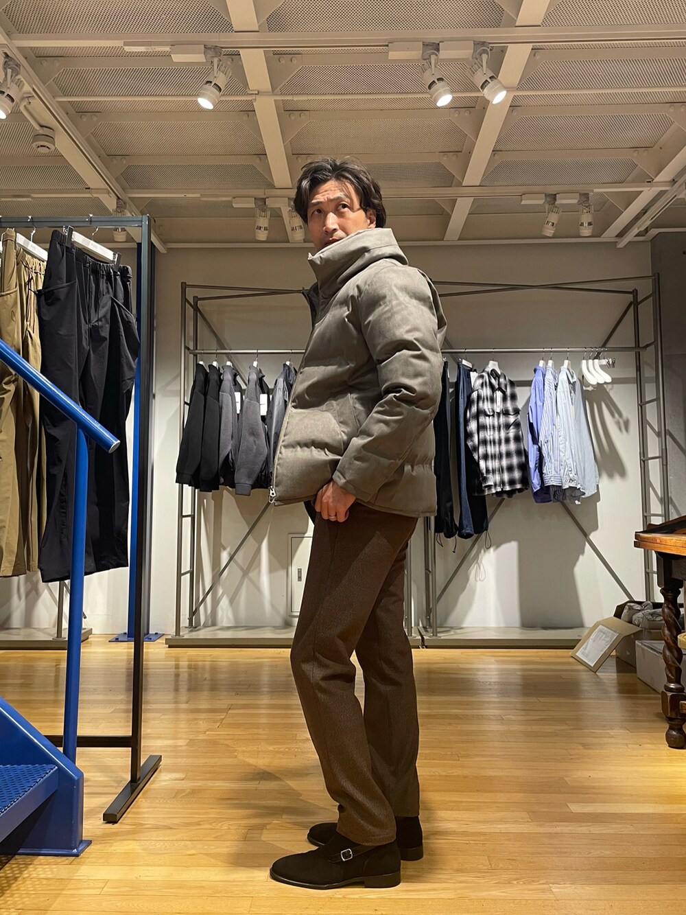 ベージュ系のダウンジャケット/コート、ブルー系のニット/セーター、ブラウン系のスラックスを着用したメンズの秋コーディネートの2枚目の写真