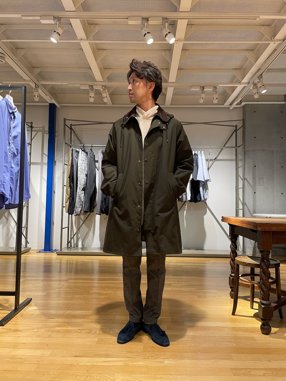 グリーン系のステンカラーコート、グレー系のスラックス、ホワイト系のパーカーを着用したメンズの秋コーディネートの3枚目の写真