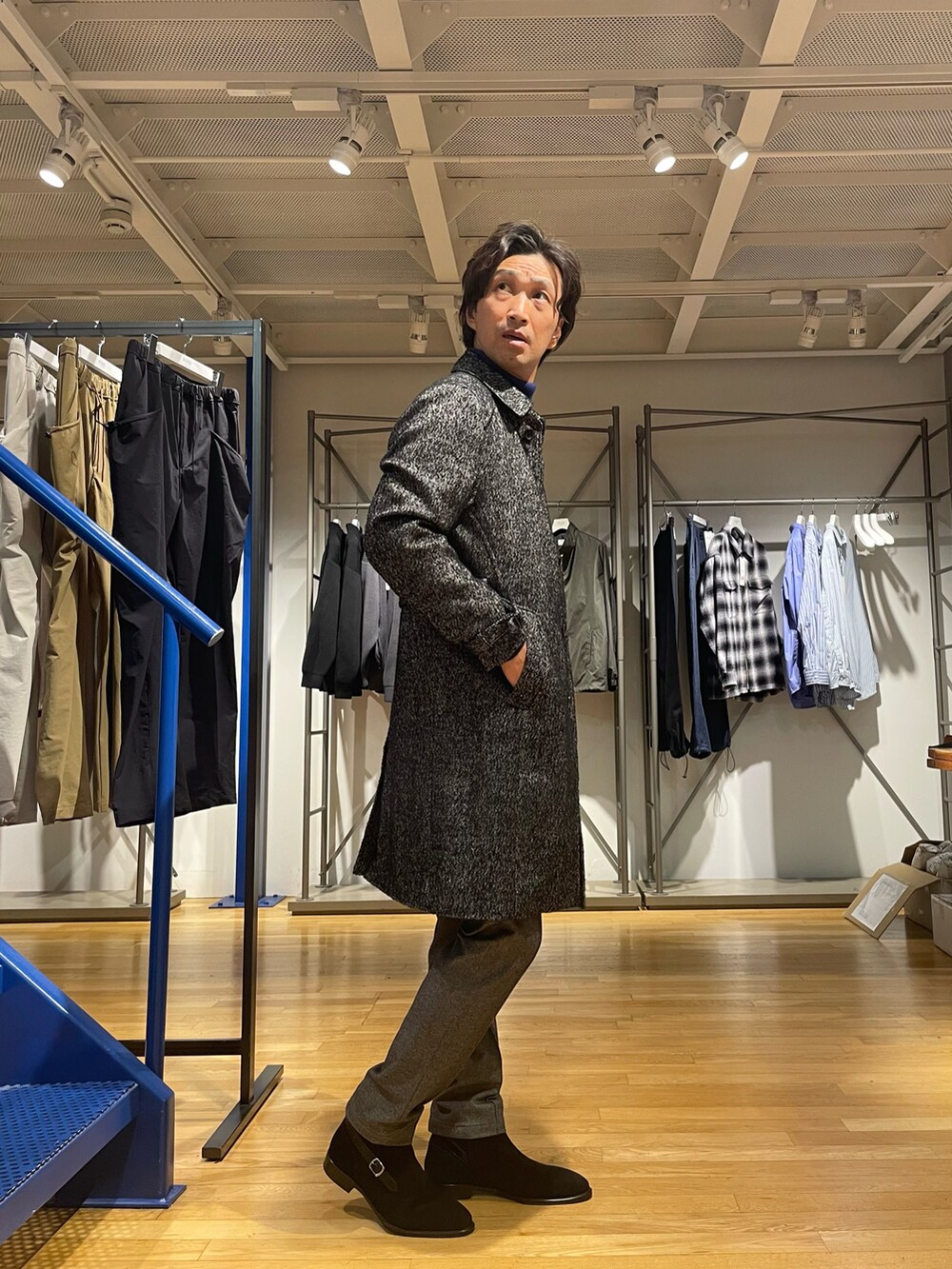 ブラック系のトレンチコート、ブルー系のニット/セーター、グレー系のスラックスを着用したメンズの秋コーディネートの2枚目の写真