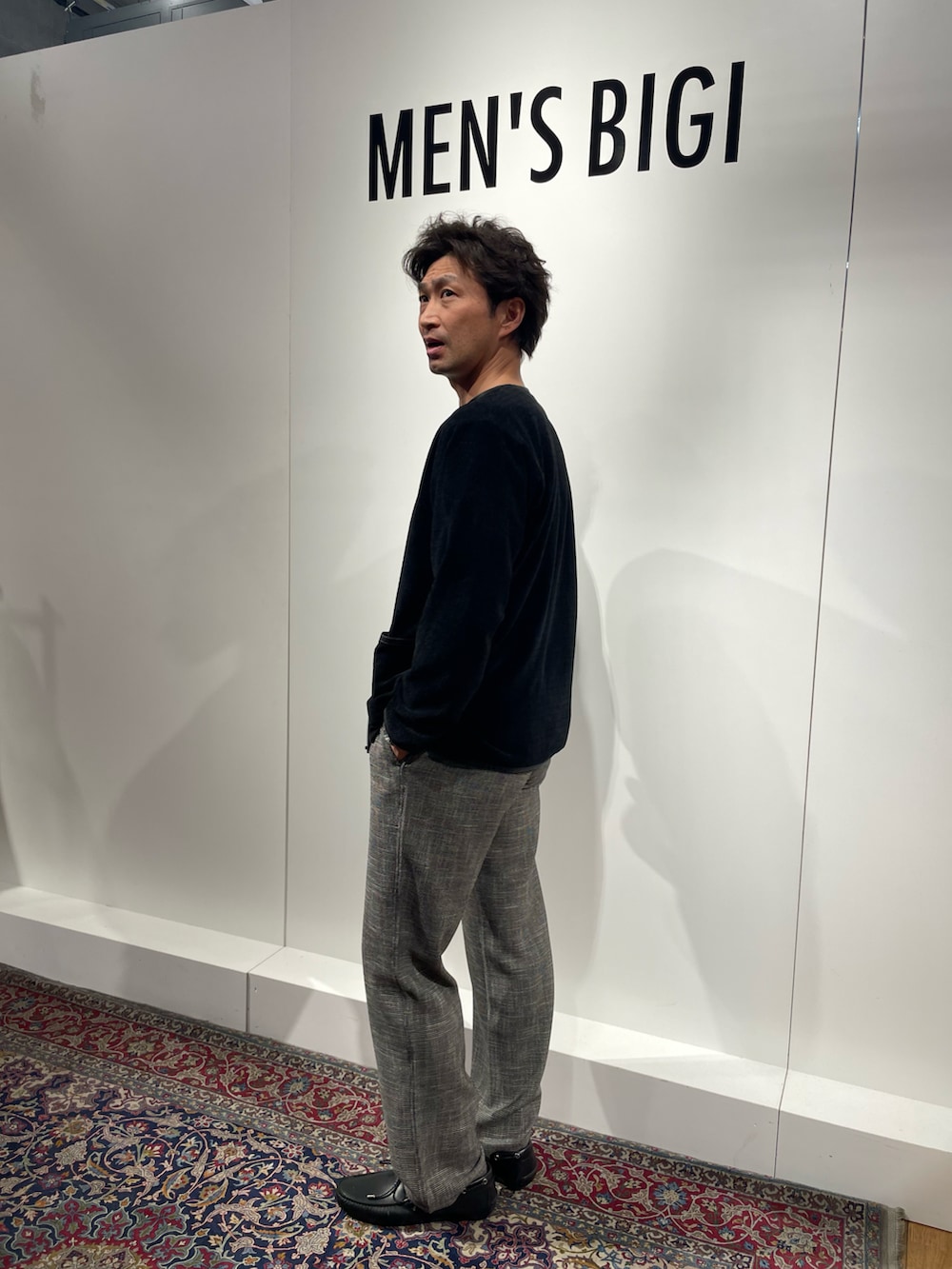 ブラック系のカーディガン/ボレロ、グレー系のパンツ、ブラック系のモカシン/デッキシューズを着用したメンズの春コーディネートの2枚目の写真