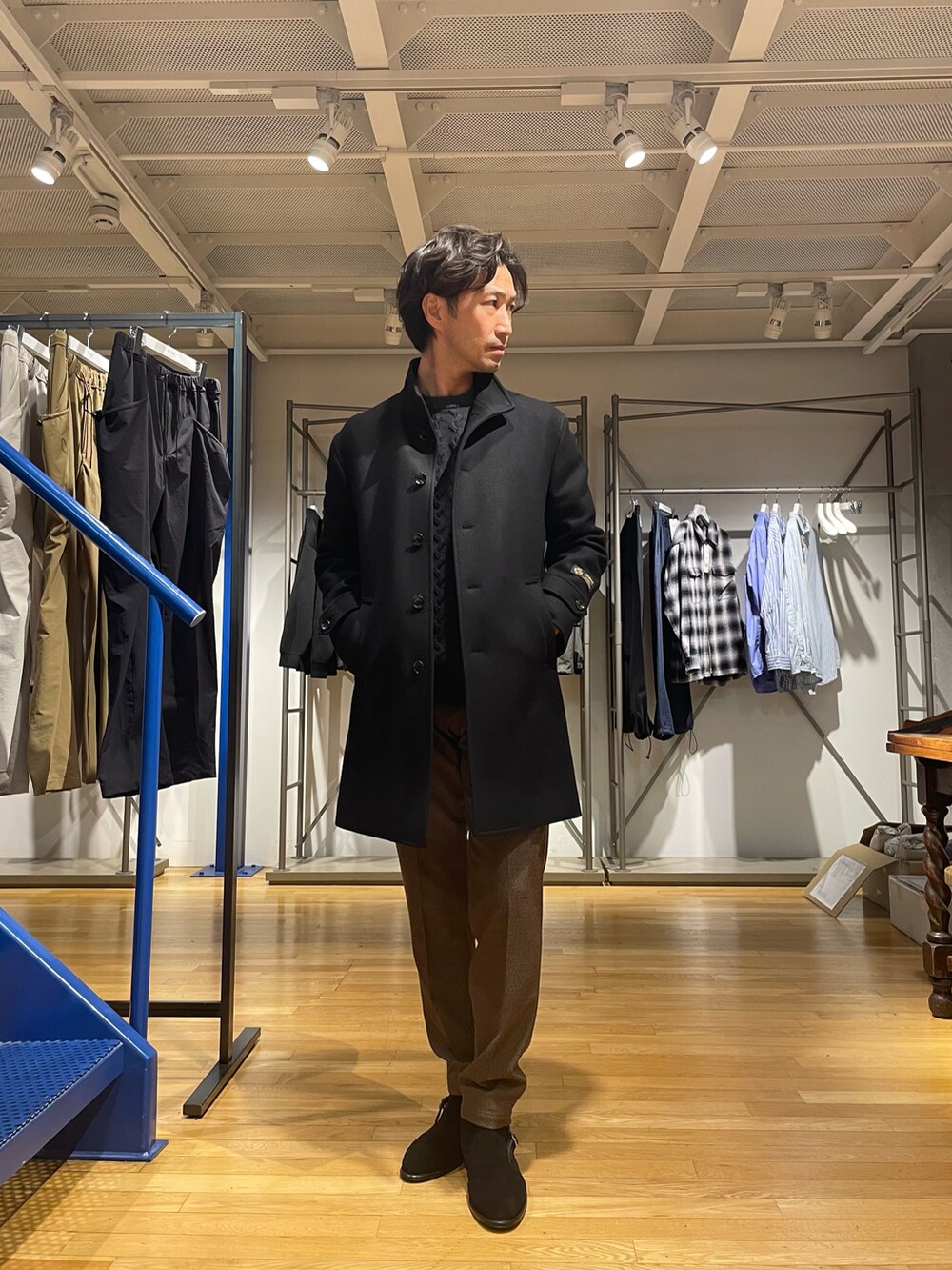 ブラック系のステンカラーコート、ブラウン系のスラックス、ブラック系のブーツを着用したメンズの秋コーディネートの2枚目の写真