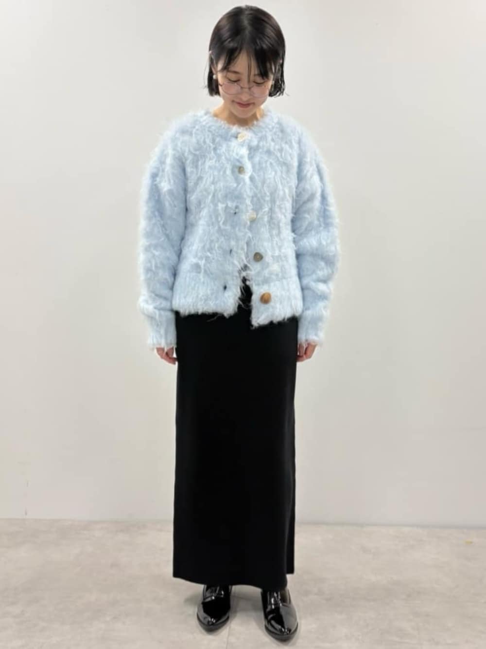 ブルー系のカーディガン/ボレロ、ブラック系のスカート、ブラック系のローファーを着用したレディースの秋コーディネートの2枚目の写真