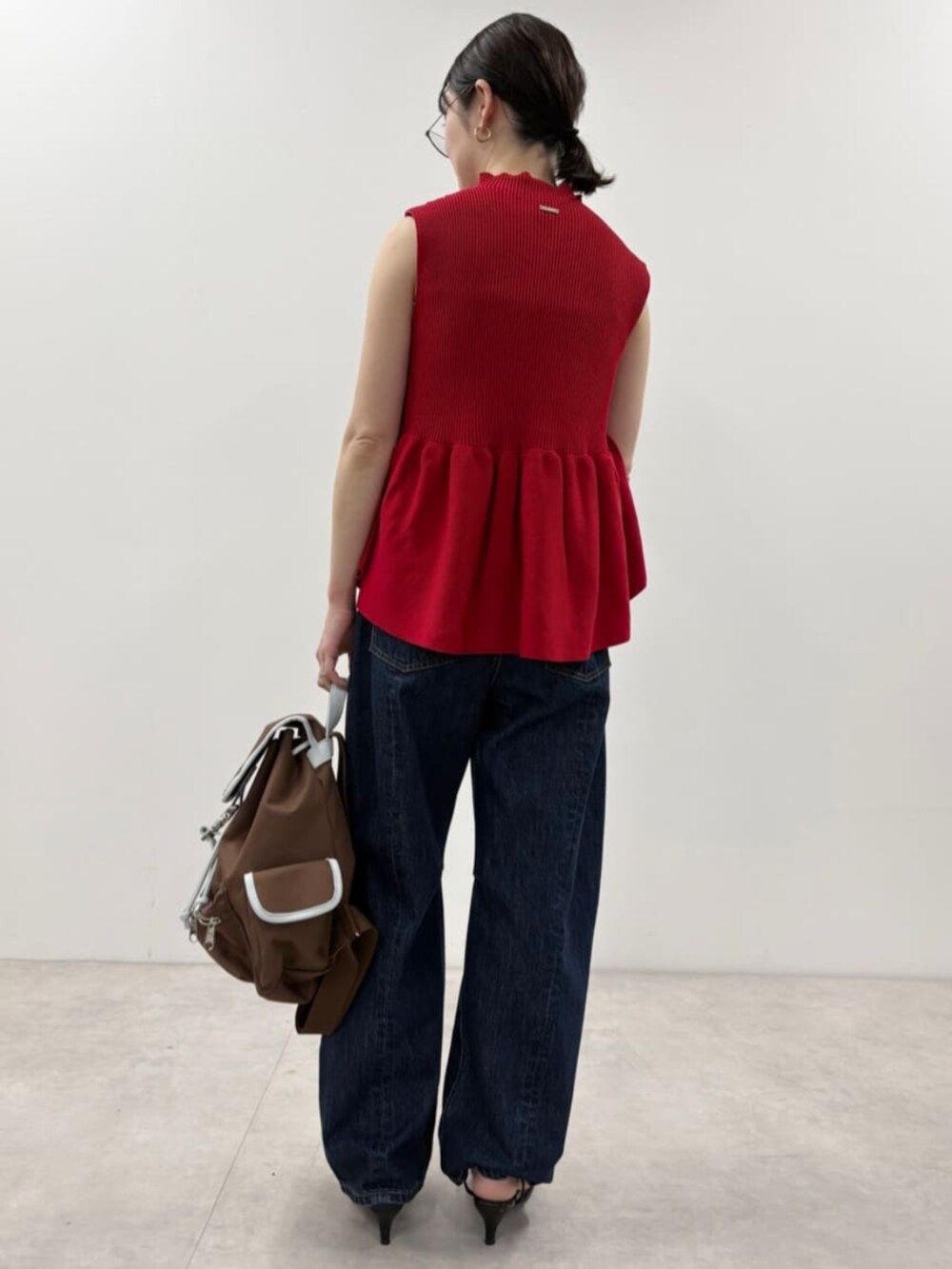 ブルー系のデニムパンツ、ブラウン系のバックパック/リュック、レッド系のベストを着用したレディースの春コーディネートの3枚目の写真