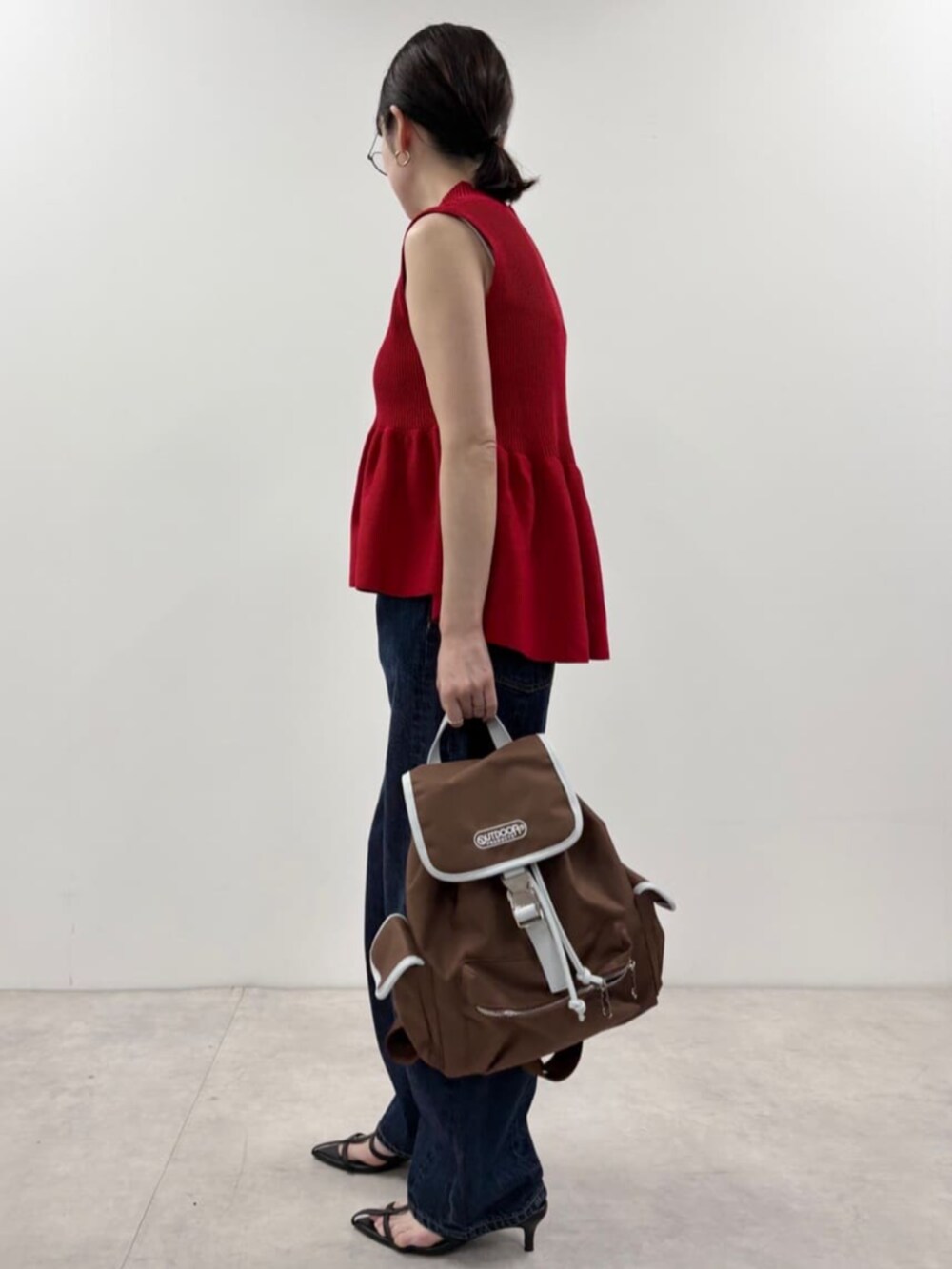 ブルー系のデニムパンツ、ブラウン系のバックパック/リュック、レッド系のベストを着用したレディースの春コーディネートの2枚目の写真