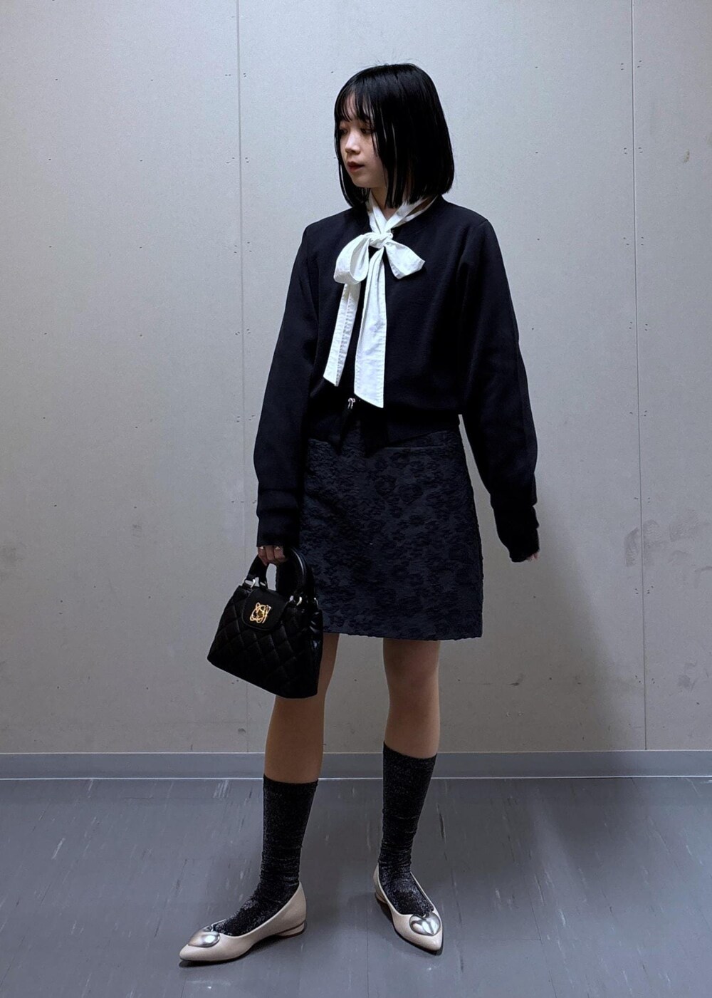 グレー系のスカート、ベージュ系のテーラードジャケット、ホワイト系のバレエシューズを着用したレディースの春コーディネートの6枚目の写真