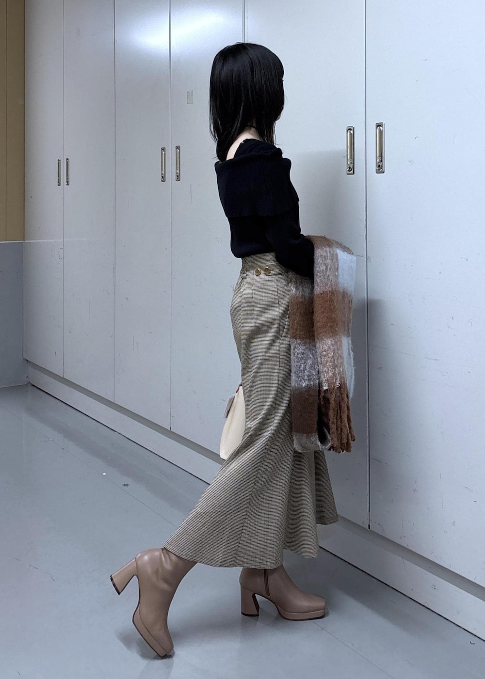 ベージュ系のショルダーバッグ、ベージュ系のスカート、ブラック系のニット/セーターを着用したレディースの冬コーディネートの2枚目の写真