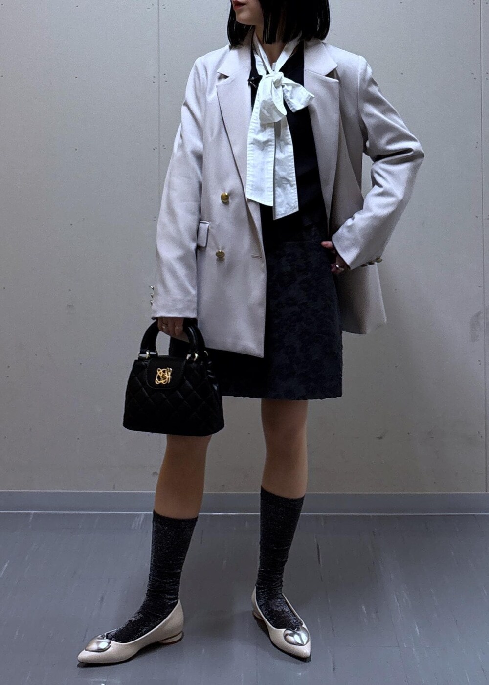 グレー系のスカート、ベージュ系のテーラードジャケット、ホワイト系のバレエシューズを着用したレディースの春コーディネートの4枚目の写真