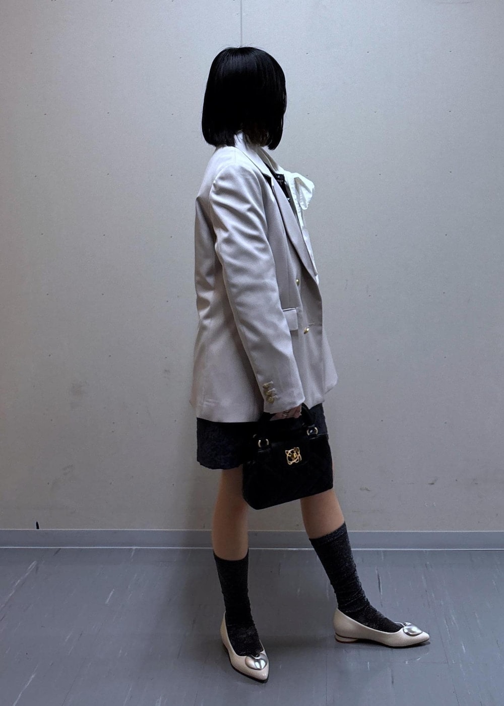 グレー系のスカート、ベージュ系のテーラードジャケット、ホワイト系のバレエシューズを着用したレディースの春コーディネートの2枚目の写真