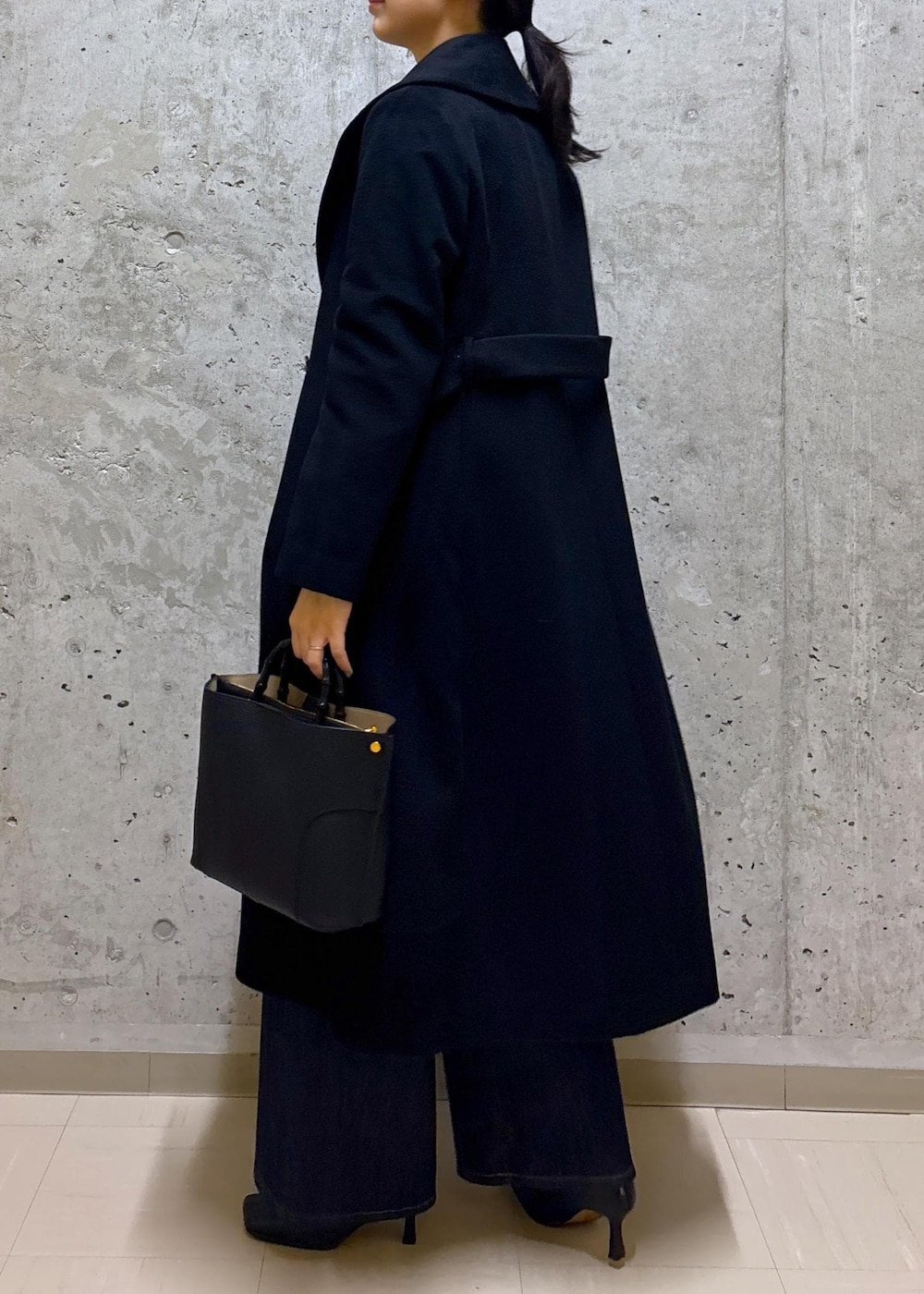 ブラック系のハンドバッグ、ブラック系のステンカラーコート、ブルー系のデニムパンツを着用したレディースの秋コーディネートの6枚目の写真