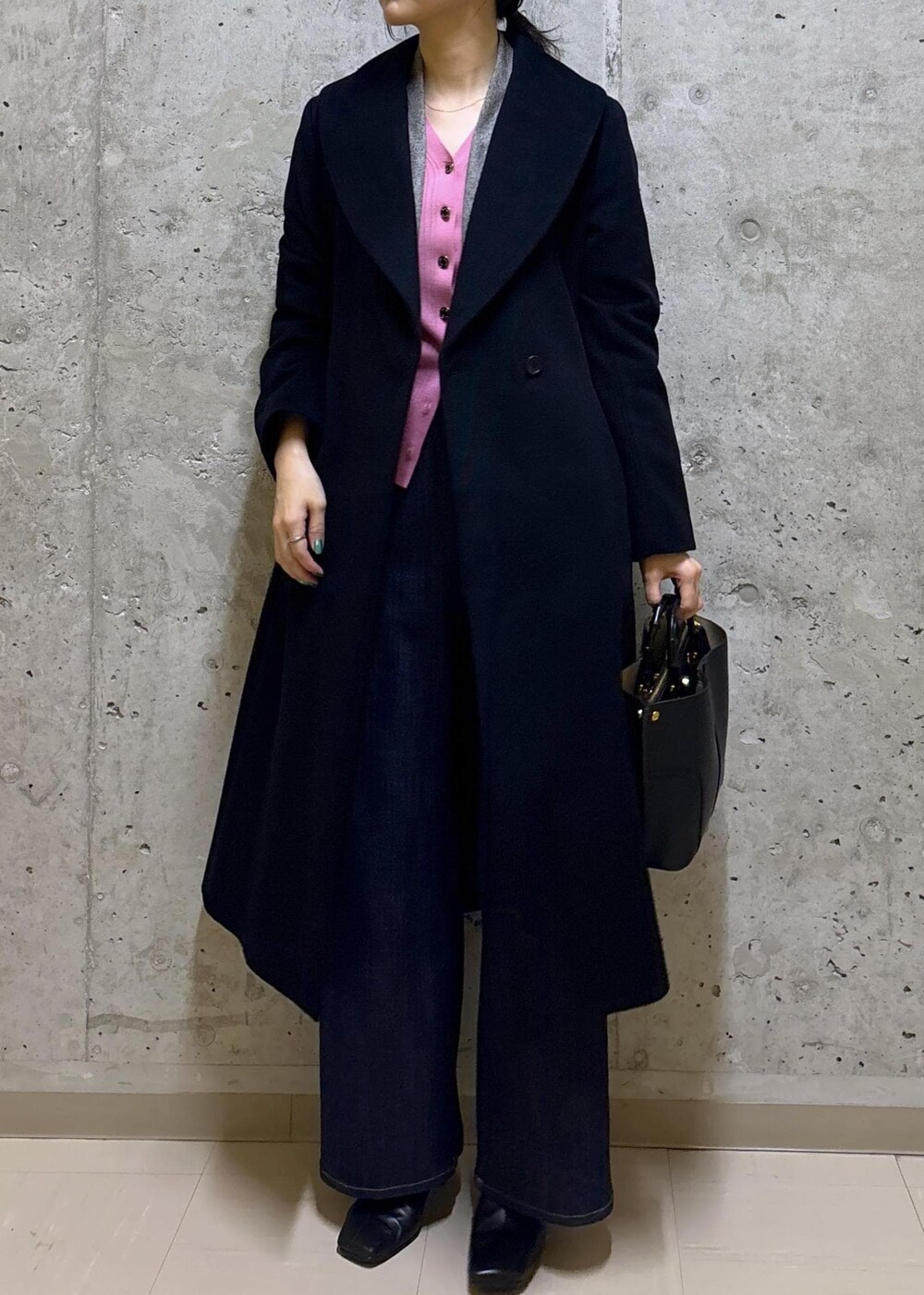 ブラック系のハンドバッグ、ブラック系のステンカラーコート、ブルー系のデニムパンツを着用したレディースの秋コーディネートの5枚目の写真