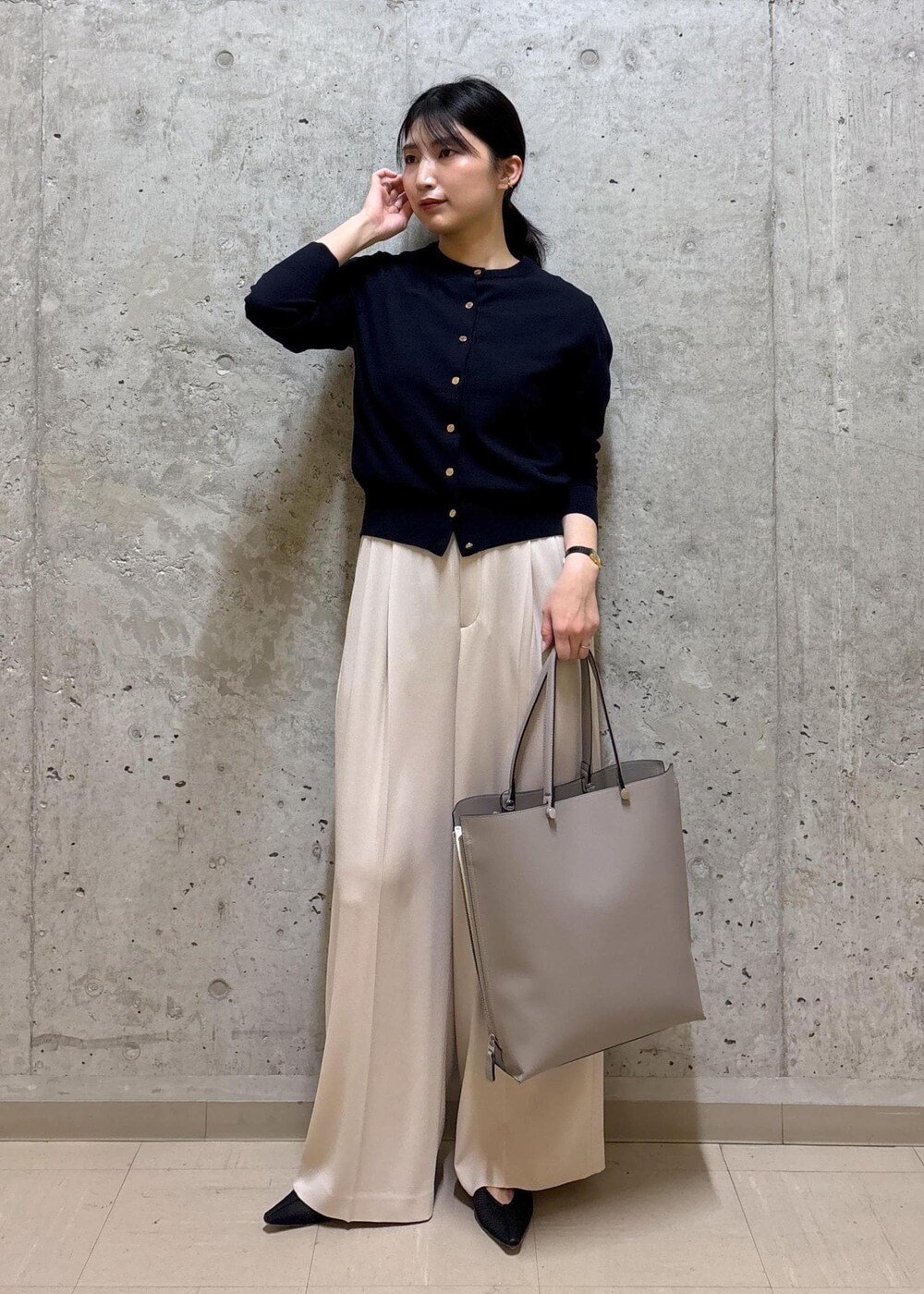 グレー系のトートバッグ、ブラック系のパンプス、ブルー系のニット/セーターを着用したレディースの春コーディネートの3枚目の写真