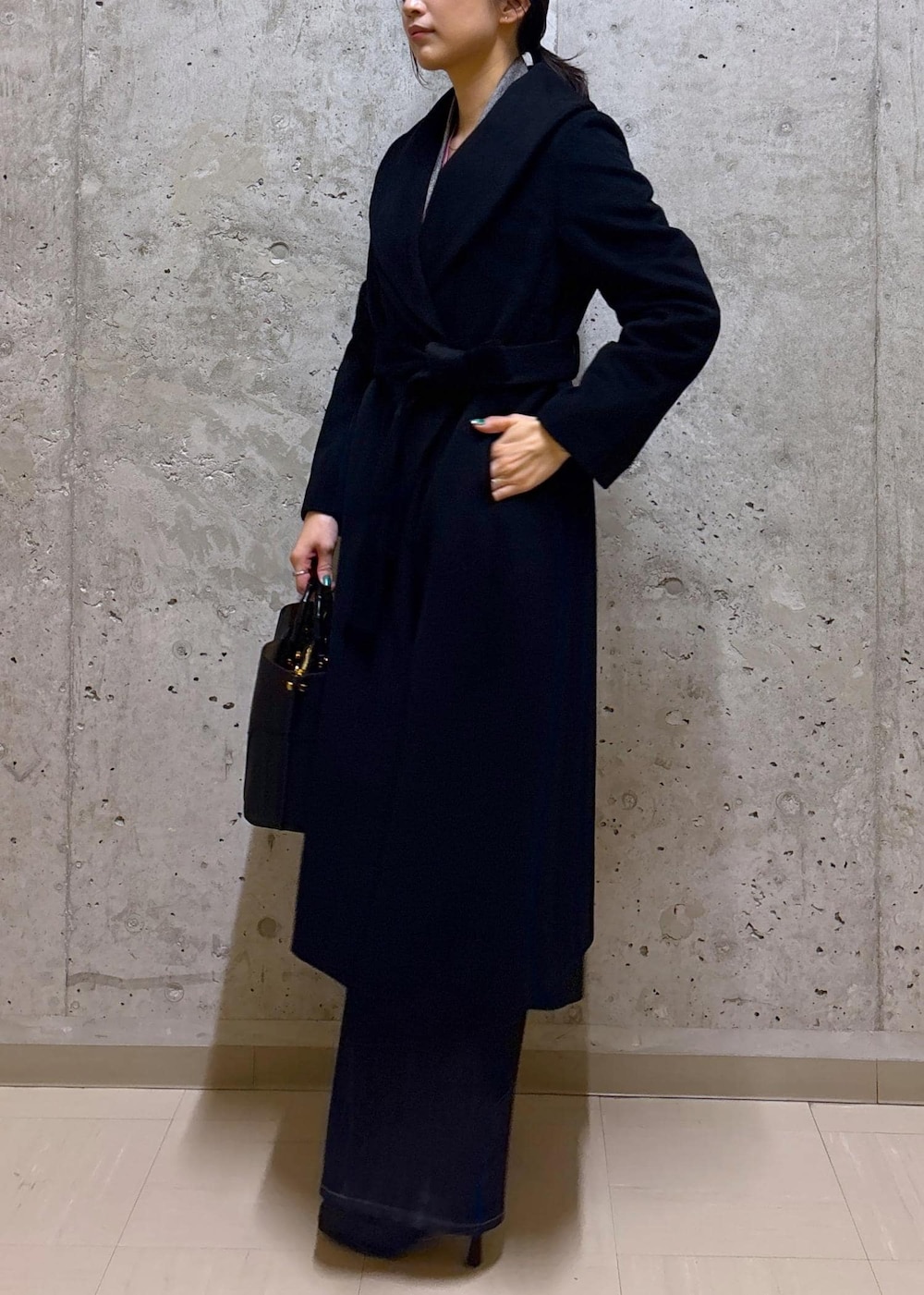 ブラック系のハンドバッグ、ブラック系のステンカラーコート、ブルー系のデニムパンツを着用したレディースの秋コーディネートの3枚目の写真