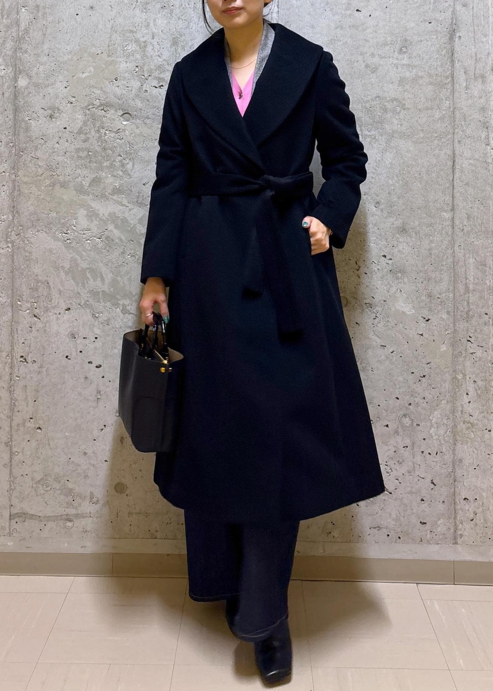 ブラック系のハンドバッグ、ブラック系のステンカラーコート、ブルー系のデニムパンツを着用したレディースの秋コーディネートの2枚目の写真