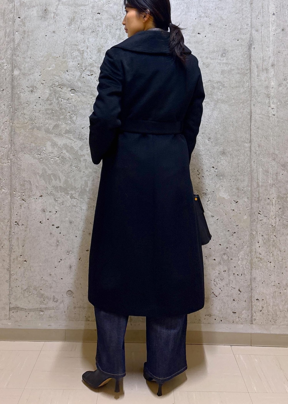 ブラック系のハンドバッグ、ブラック系のステンカラーコート、ブルー系のデニムパンツを着用したレディースの秋コーディネートの4枚目の写真