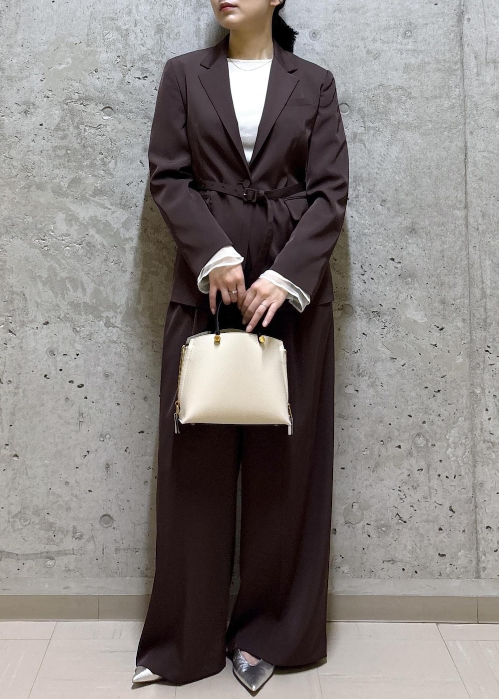 シルバー系のパンプス、ホワイト系のハンドバッグ、ブラウン系のテーラードジャケットを着用したレディースの春コーディネートの2枚目の写真