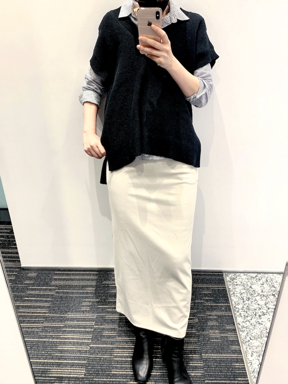 ブラック系のベスト、ベージュ系のスカート、ブラック系のブーツを着用したレディースの春コーディネートの2枚目の写真