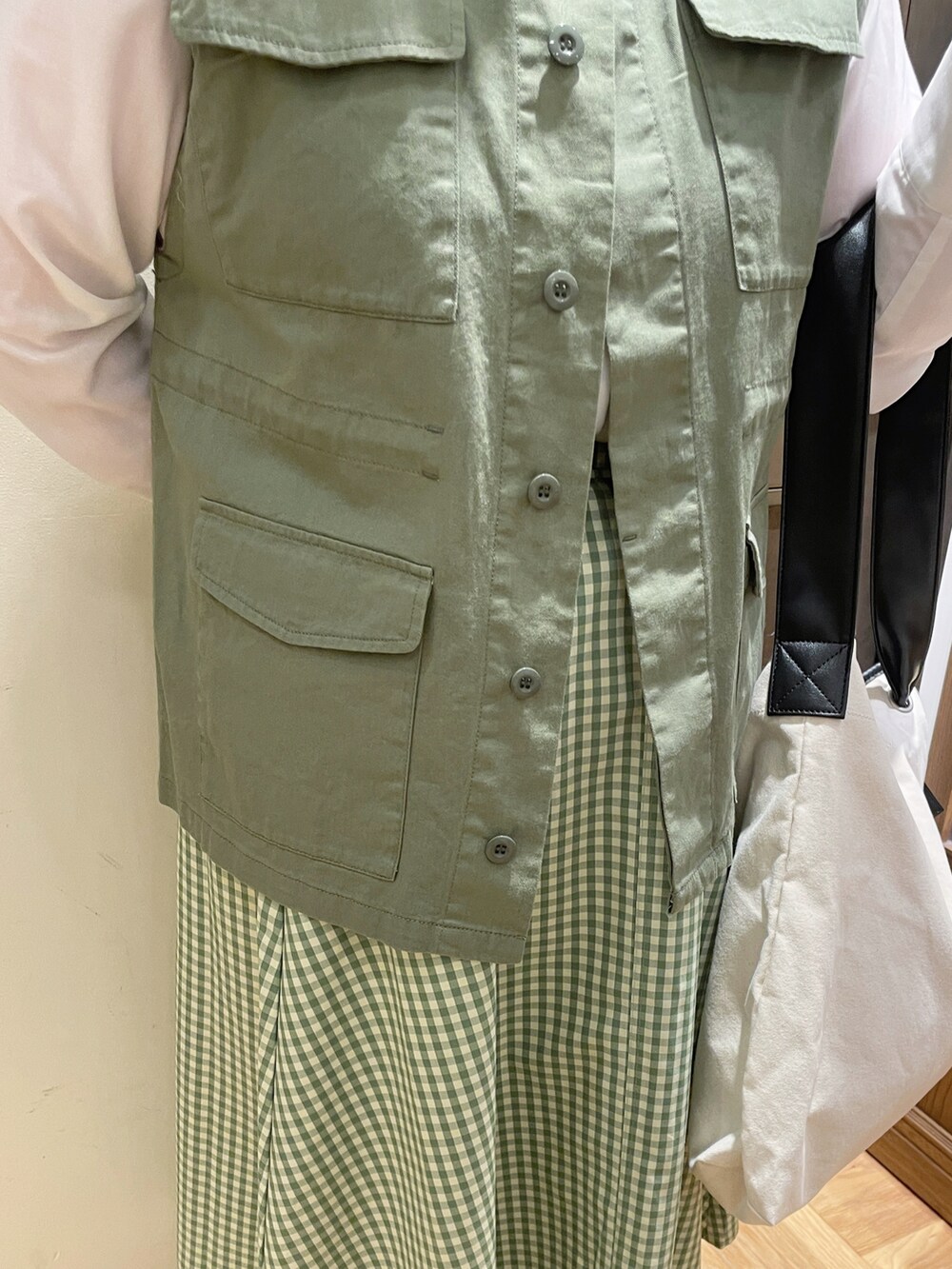 グリーン系のベスト、ブラック系のハンドバッグ、ブラック系のドレスシューズを着用したレディースの春コーディネートの2枚目の写真