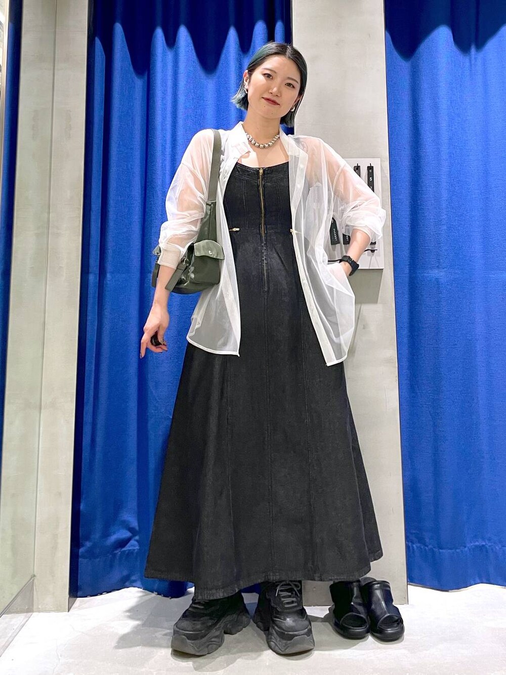 グリーン系のショルダーバッグ、ブラック系のスニーカー、ブラック系のワンピースを着用したレディースの春コーディネートの2枚目の写真