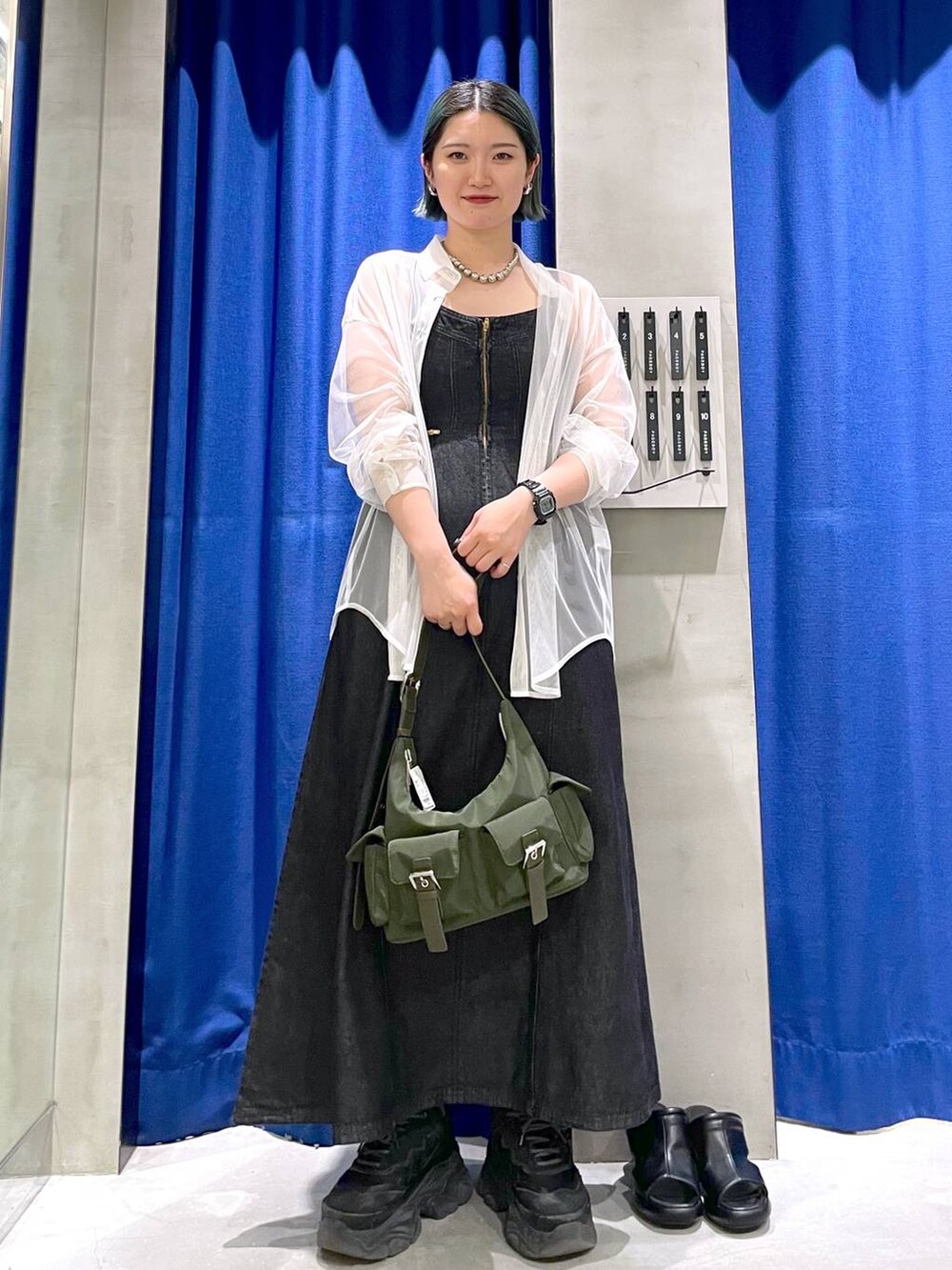 グリーン系のショルダーバッグ、ブラック系のスニーカー、ブラック系のワンピースを着用したレディースの春コーディネートの3枚目の写真