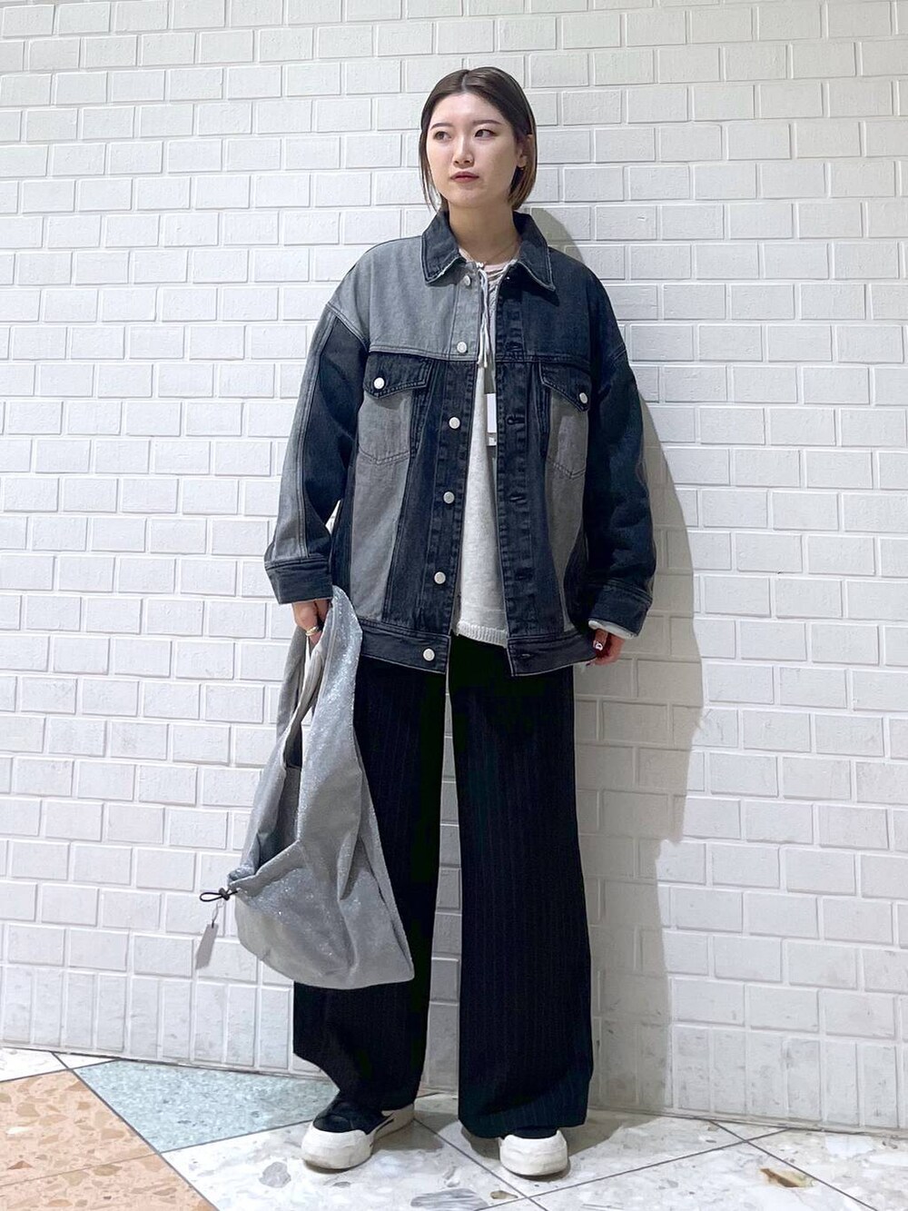 ブラック系のスラックス、グレー系のニット/セーター、ブラック系のデニムジャケットを着用したレディースの春コーディネートの2枚目の写真