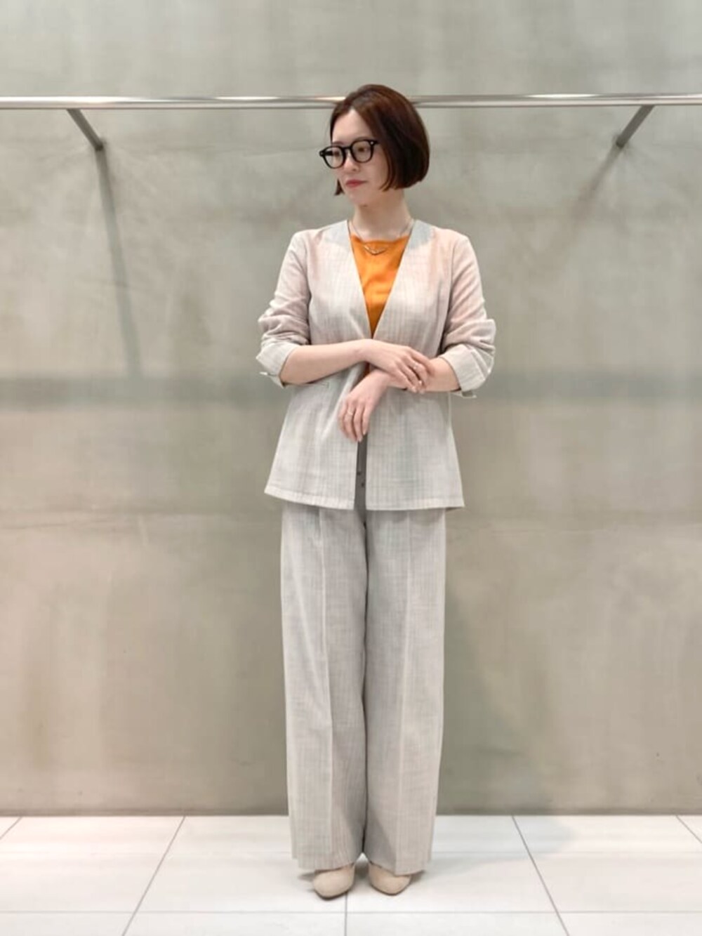 オレンジ系のニット/セーター、ホワイト系のノーカラージャケット、ホワイト系のスラックスを着用したレディースの春コーディネートの2枚目の写真