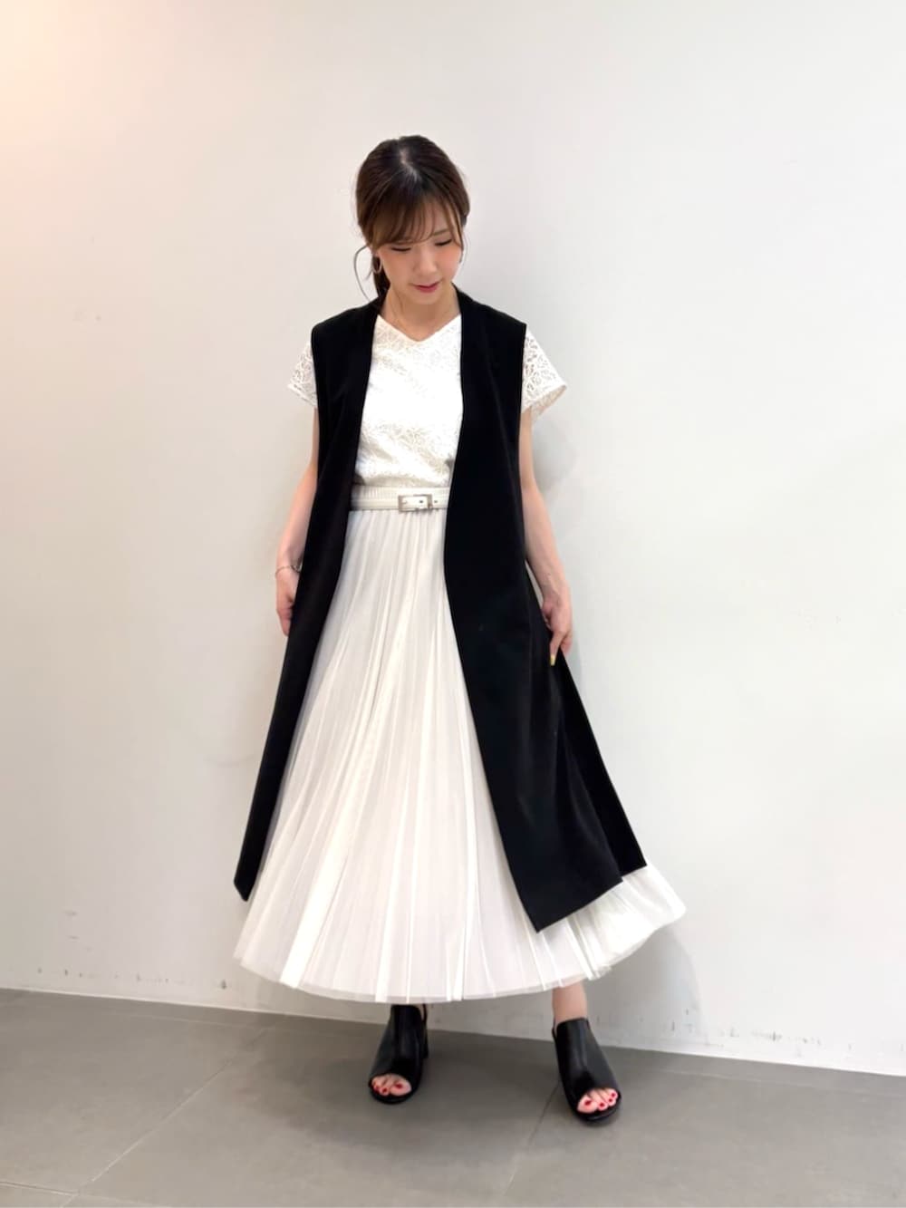 グレー系のスカート、ブラック系のサンダル、ブラック系のベストを着用したレディースの春コーディネートの4枚目の写真