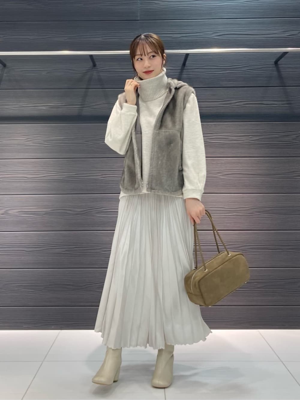 ベージュ系のベスト、ホワイト系のブーツ、ホワイト系のスカートを着用したレディースの秋コーディネートの2枚目の写真