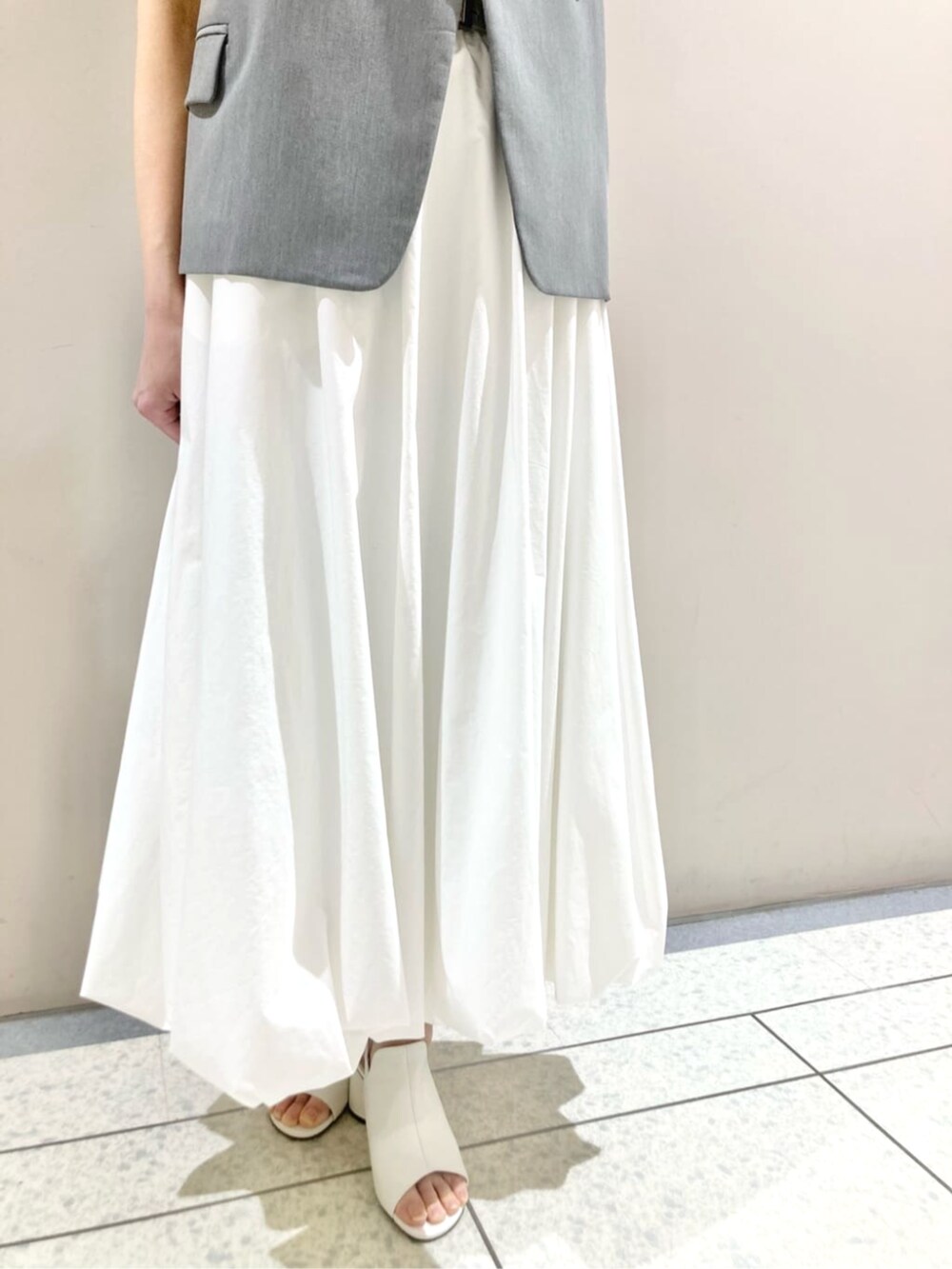 ホワイト系のスカート、ブラック系のベスト、ホワイト系のサンダルを着用したレディースの春コーディネートの6枚目の写真