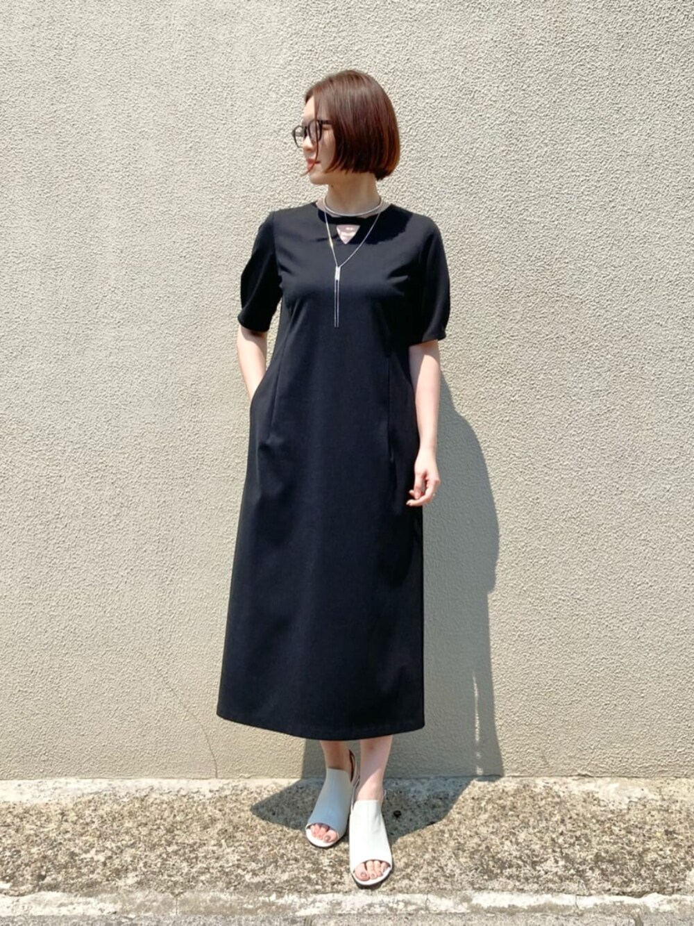 ホワイト系のサンダル、ブラック系のワンピース、シルバー系のネックレスを着用したレディースの春コーディネートの2枚目の写真