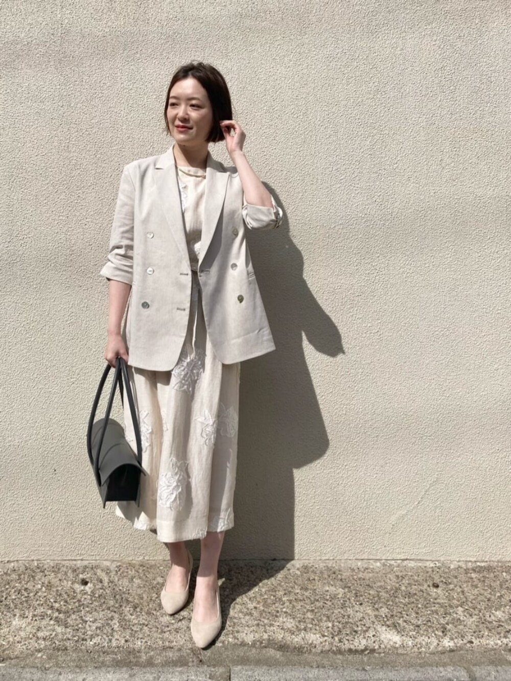 ベージュ系のテーラードジャケット、ベージュ系のワンピース、ゴールド系のネックレスを着用したレディースの夏コーディネートの2枚目の写真