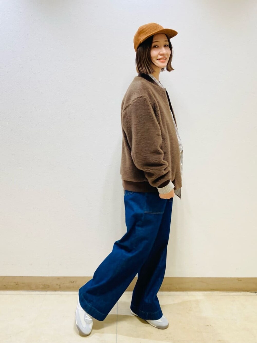 ブラウン系のブルゾン、ブルー系のデニムパンツ、イエロー系のキャップを着用したレディースの秋コーディネートの3枚目の写真