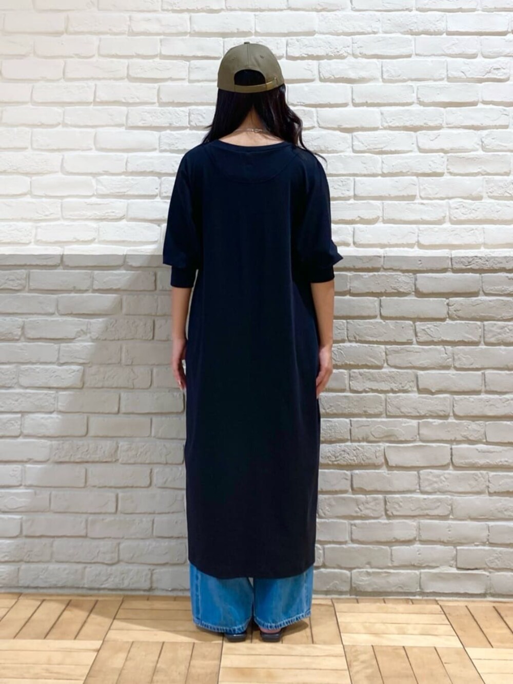 ブラック系のワンピース、ブルー系のデニムパンツ、グリーン系のキャップを着用したレディースの秋コーディネートの4枚目の写真