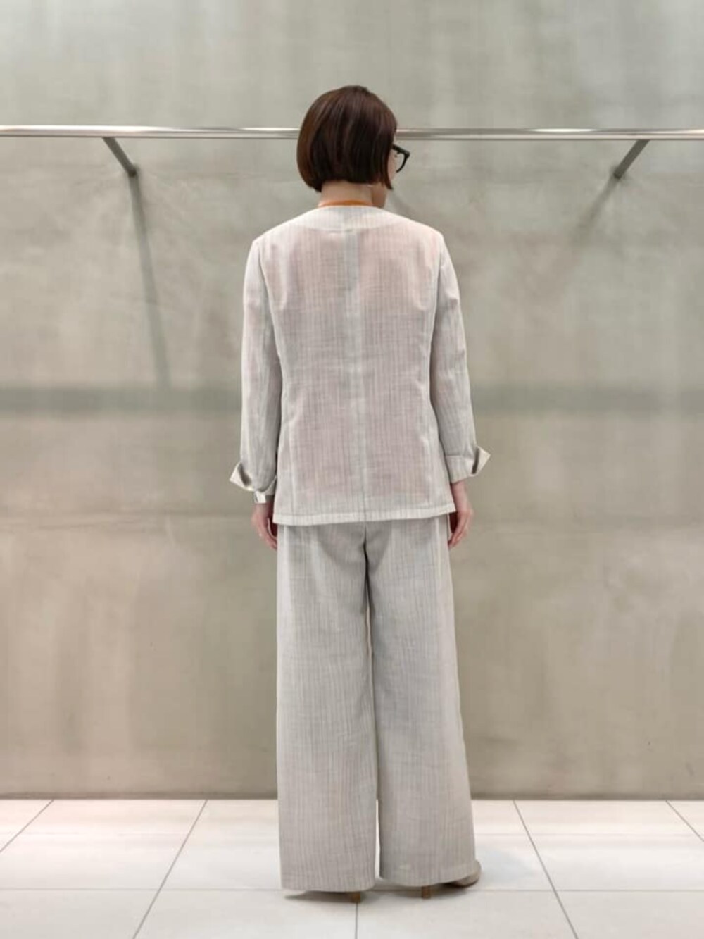 オレンジ系のニット/セーター、ホワイト系のノーカラージャケット、ホワイト系のスラックスを着用したレディースの春コーディネートの4枚目の写真