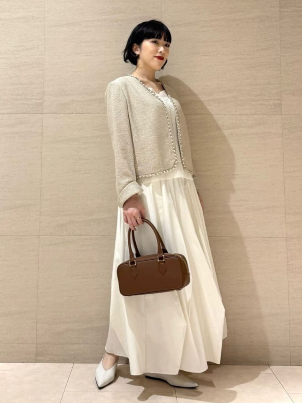 ホワイト系のパンプス、ブラウン系のボストンバッグ、ゴールド系のネックレスを着用したレディースの春コーディネートの3枚目の写真
