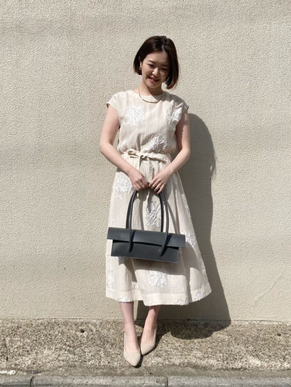 ベージュ系のテーラードジャケット、ベージュ系のワンピース、ゴールド系のネックレスを着用したレディースの夏コーディネートの4枚目の写真