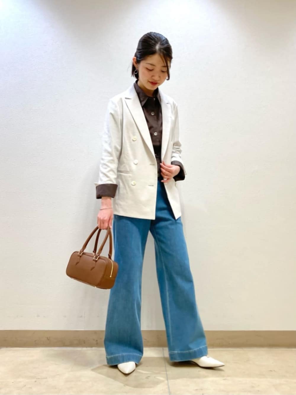 ブルー系のデニムパンツ、ホワイト系のテーラードジャケット、ブラック系のボストンバッグを着用したレディースの春コーディネートの2枚目の写真