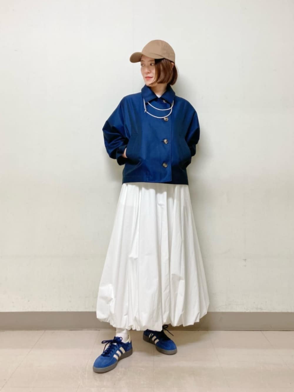 ホワイト系のスカート、ブルー系のブルゾン、イエロー系のキャップを着用したレディースの春コーディネートの2枚目の写真