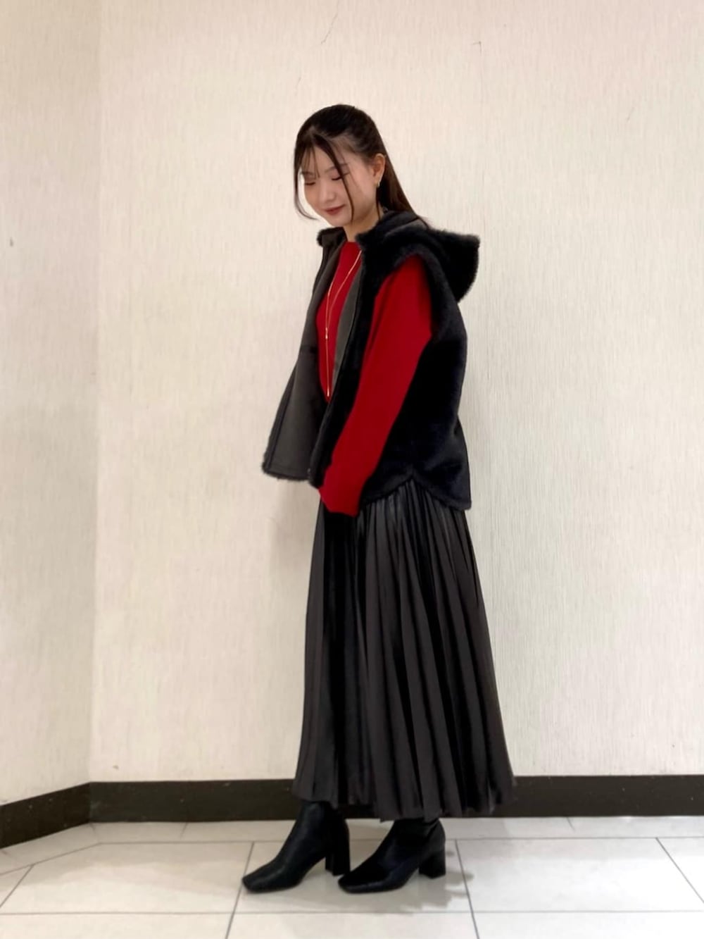 グレー系のベスト、グレー系のスカート、レッド系のニット/セーターを着用したレディースの秋コーディネートの3枚目の写真