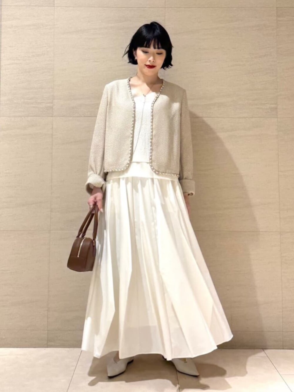 ホワイト系のパンプス、ブラウン系のボストンバッグ、ゴールド系のネックレスを着用したレディースの春コーディネートの2枚目の写真