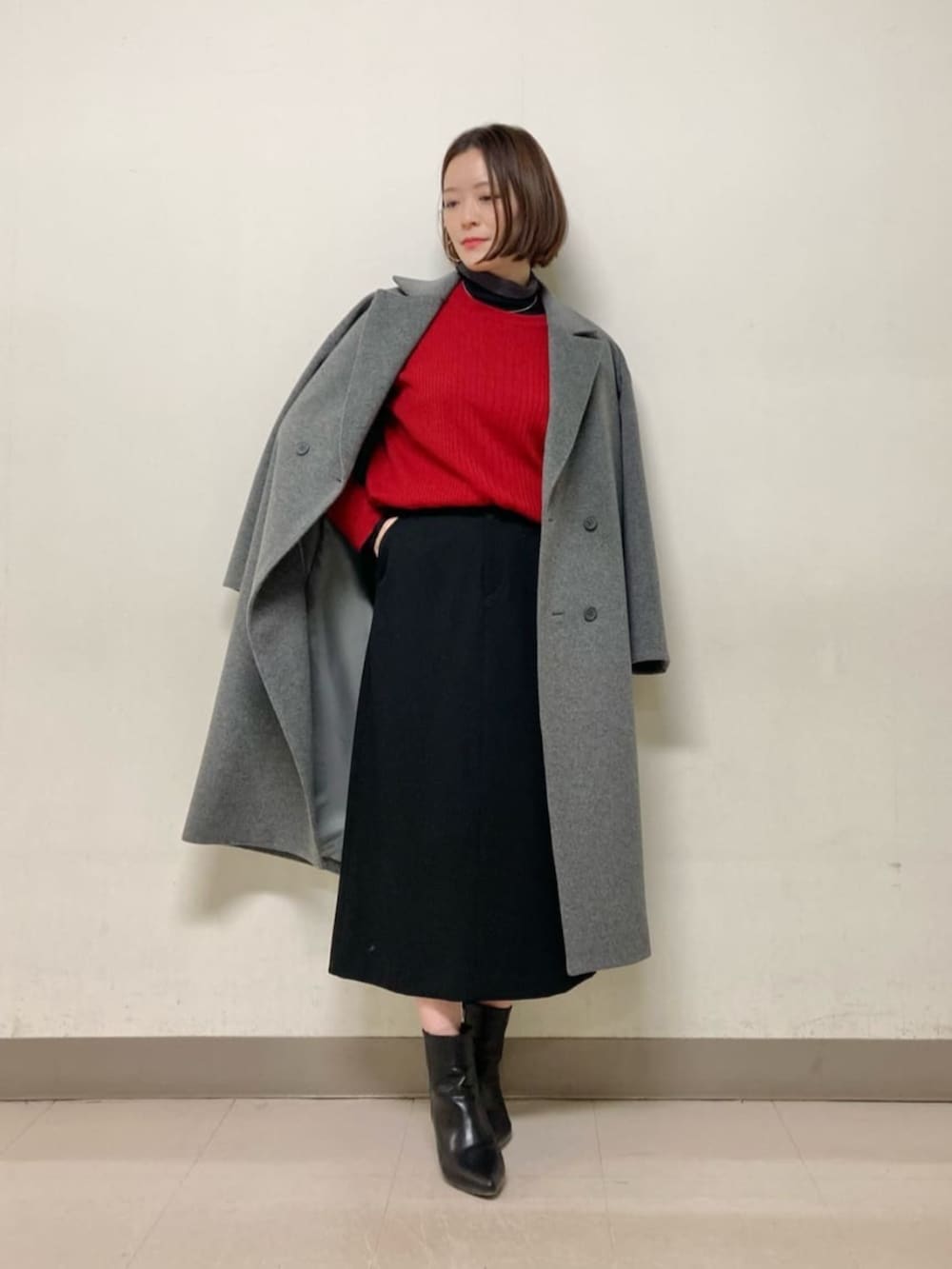 レッド系のニット/セーター、ブラック系のスカート、グレー系のチェスターコートを着用したレディースの冬コーディネートの2枚目の写真