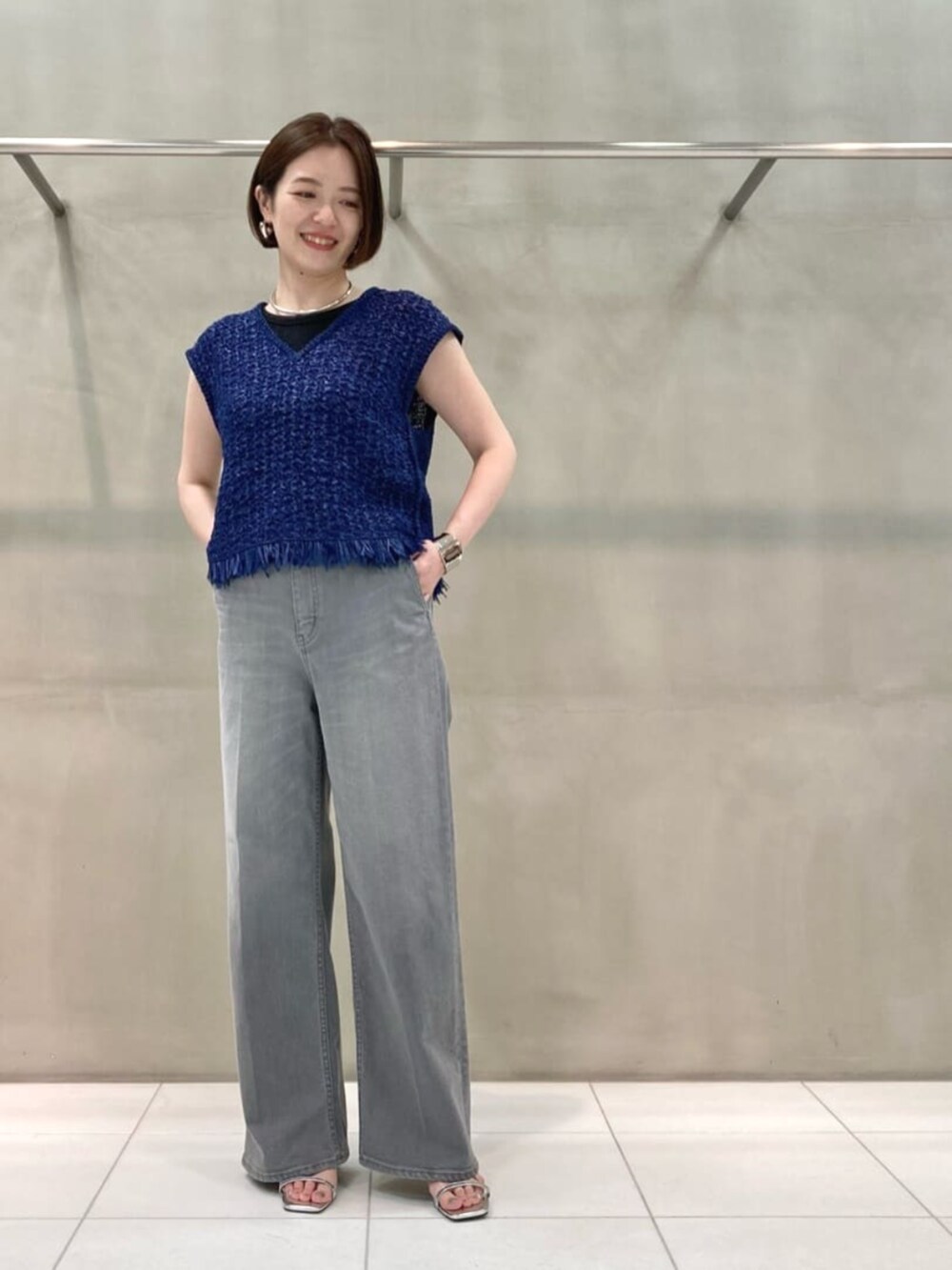 グレー系のデニムパンツ、ブルー系のニット/セーター、シルバー系のブレスレットを着用したレディースの春コーディネートの2枚目の写真