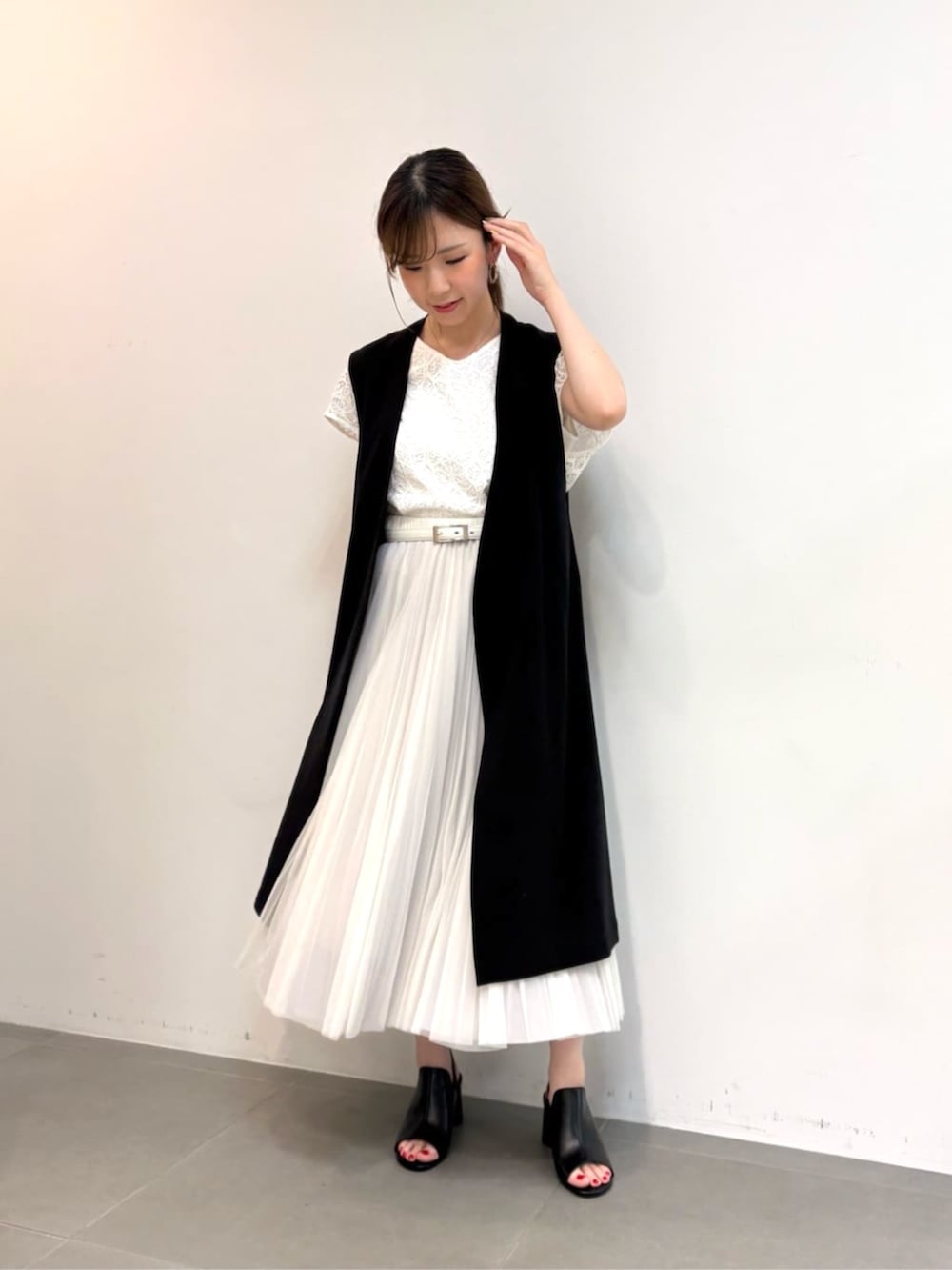 グレー系のスカート、ブラック系のサンダル、ブラック系のベストを着用したレディースの春コーディネートの2枚目の写真