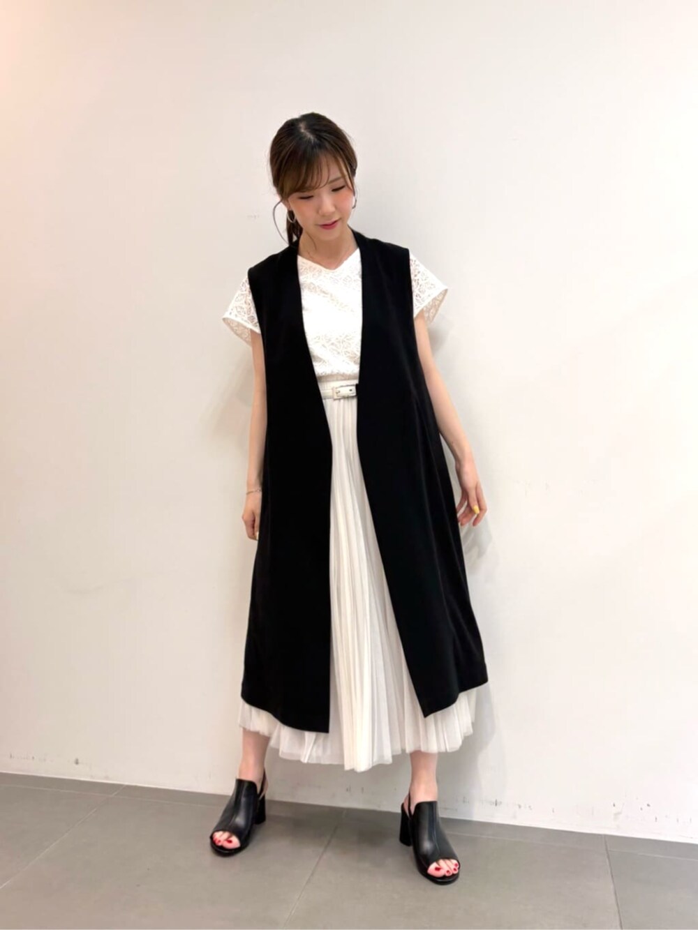 グレー系のスカート、ブラック系のサンダル、ブラック系のベストを着用したレディースの春コーディネートの3枚目の写真