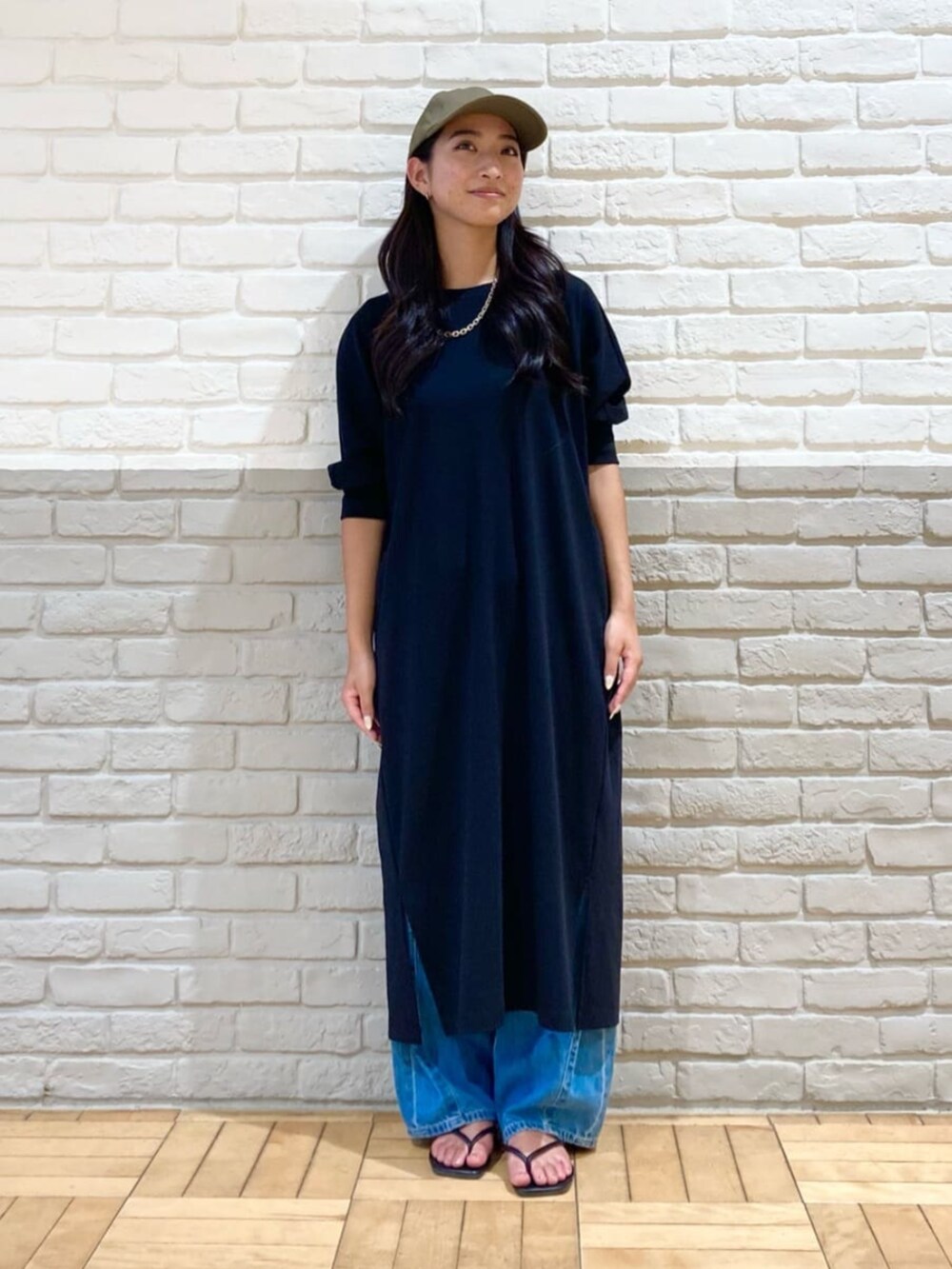 ブラック系のワンピース、ブルー系のデニムパンツ、グリーン系のキャップを着用したレディースの秋コーディネートの2枚目の写真