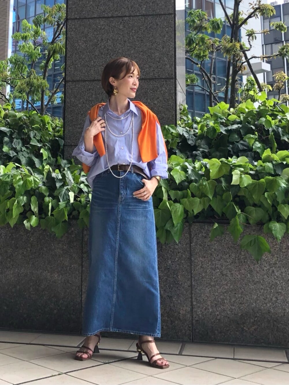 オレンジ系のニット/セーター、ブルー系のシャツ/ブラウス、ブルー系のスカートを着用したレディースの春コーディネートの5枚目の写真