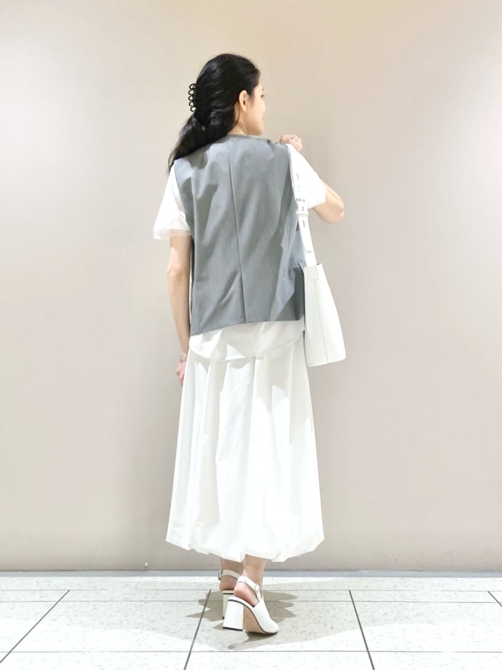 ホワイト系のスカート、ブラック系のベスト、ホワイト系のサンダルを着用したレディースの春コーディネートの3枚目の写真