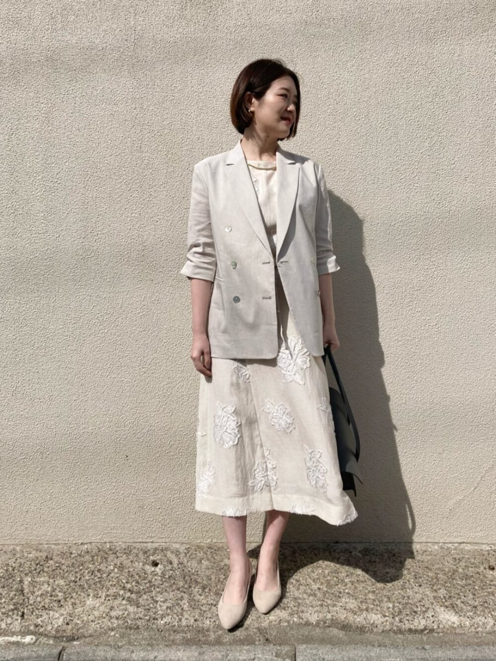 ベージュ系のテーラードジャケット、ベージュ系のワンピース、ゴールド系のネックレスを着用したレディースの夏コーディネートの3枚目の写真