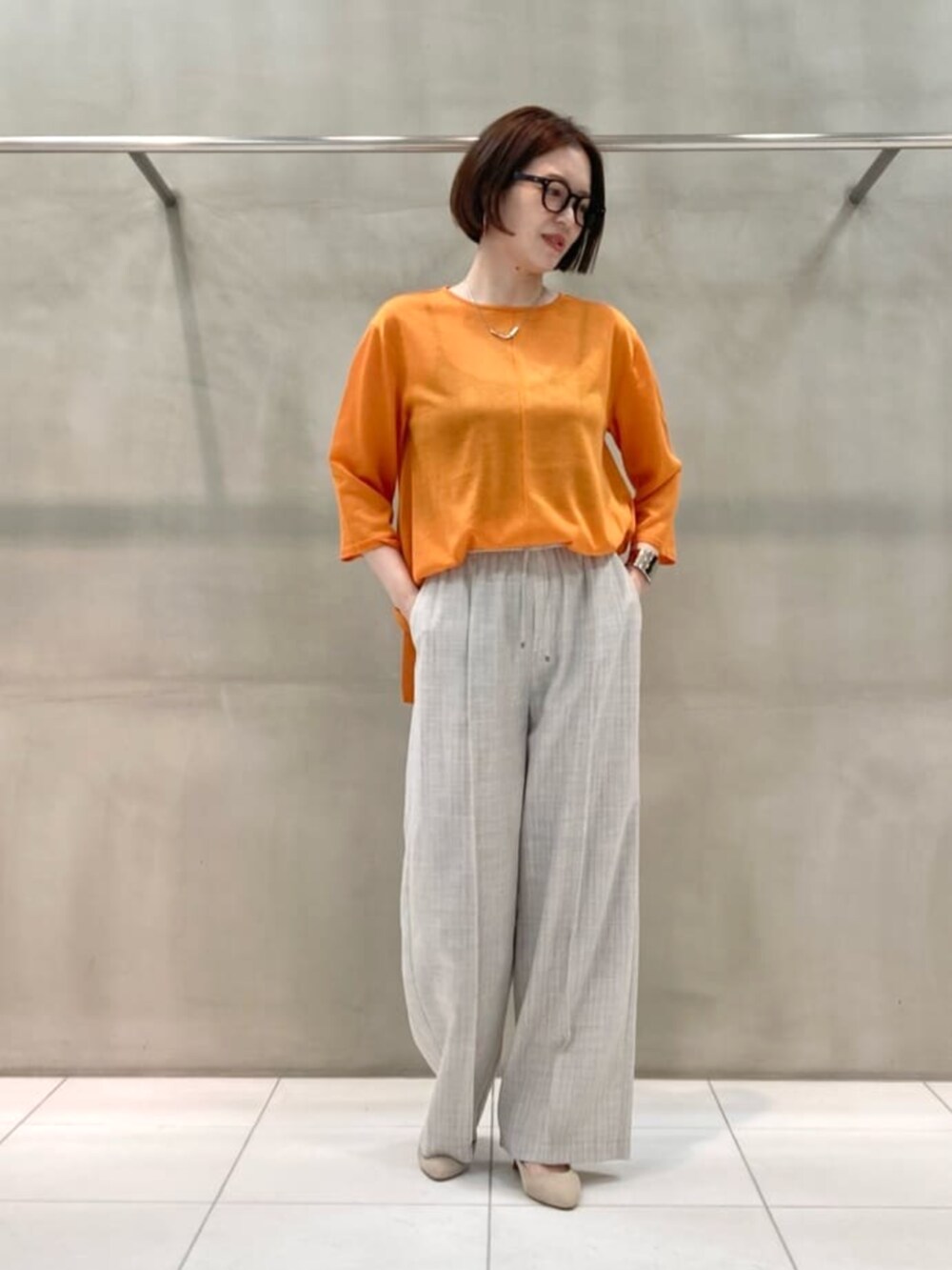 オレンジ系のニット/セーター、ホワイト系のノーカラージャケット、ホワイト系のスラックスを着用したレディースの春コーディネートの6枚目の写真